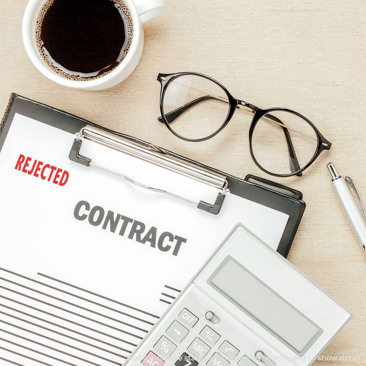 Clipboard with a contract stamped REJECTED using a Large Rejected Rubber Stamp, next to glasses, a pen, a calculator, and a cup of coffee.