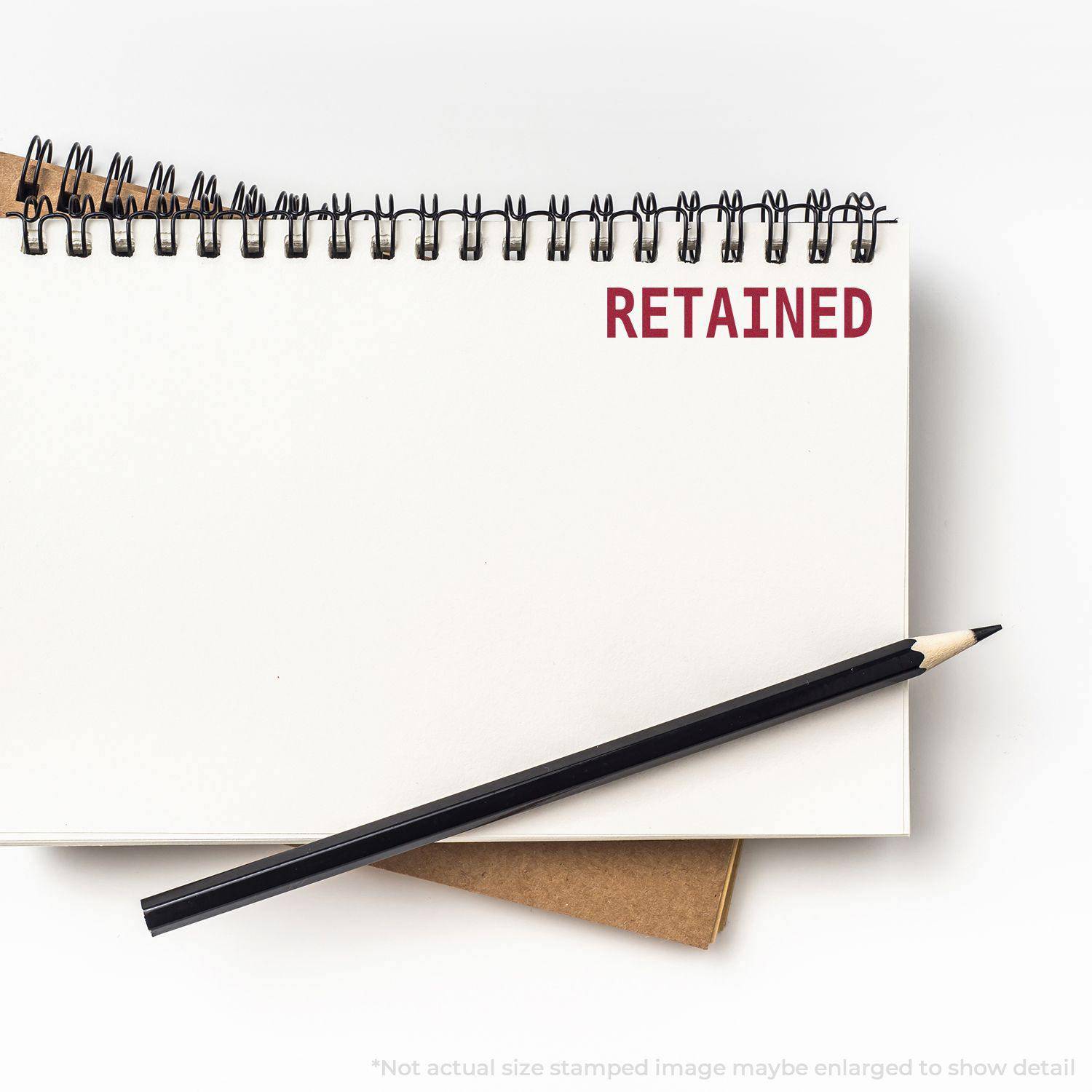 A Large Retained Rubber Stamp marks the word RETAINED in red ink on a white notebook page, with a black pencil placed diagonally.
