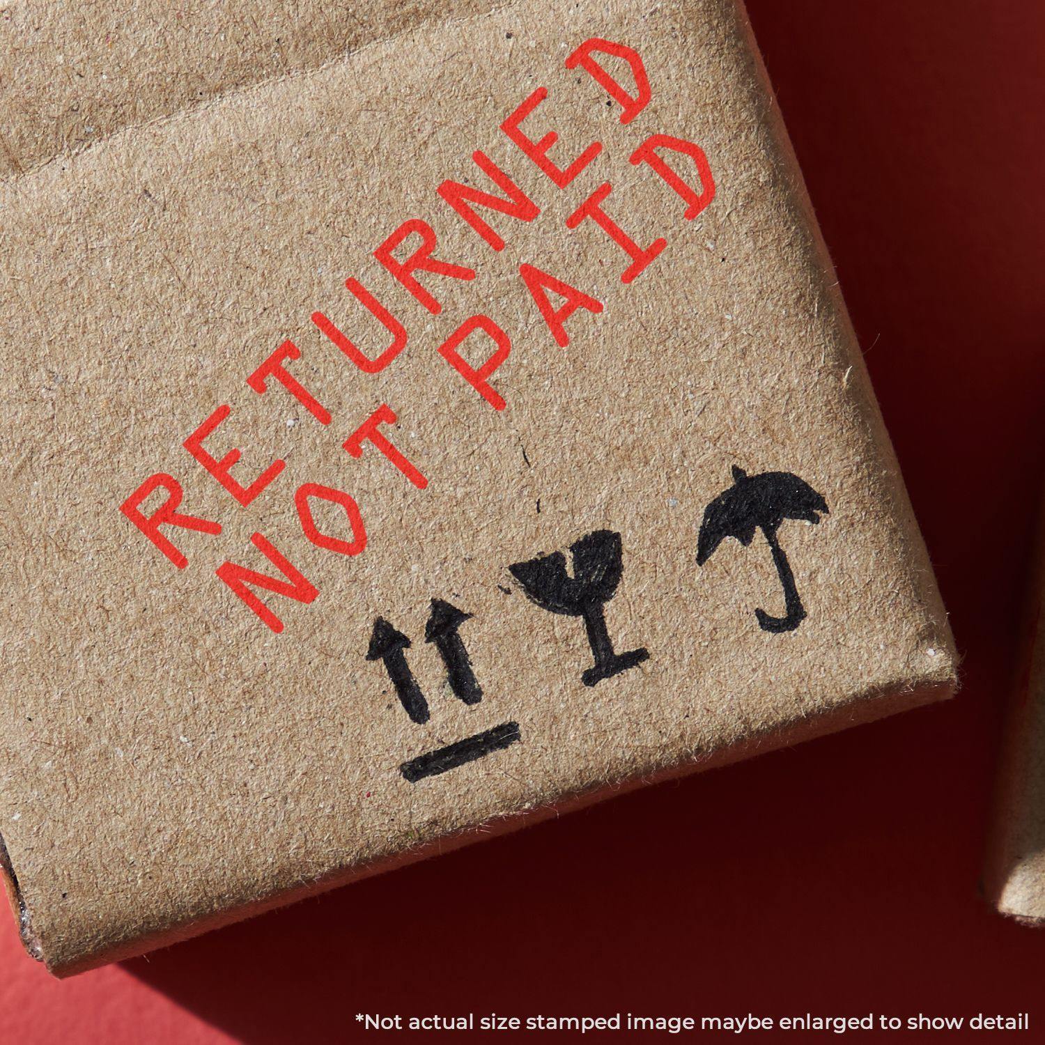 Returned Not Paid rubber stamp in red ink on a cardboard package with shipping symbols, close-up view.