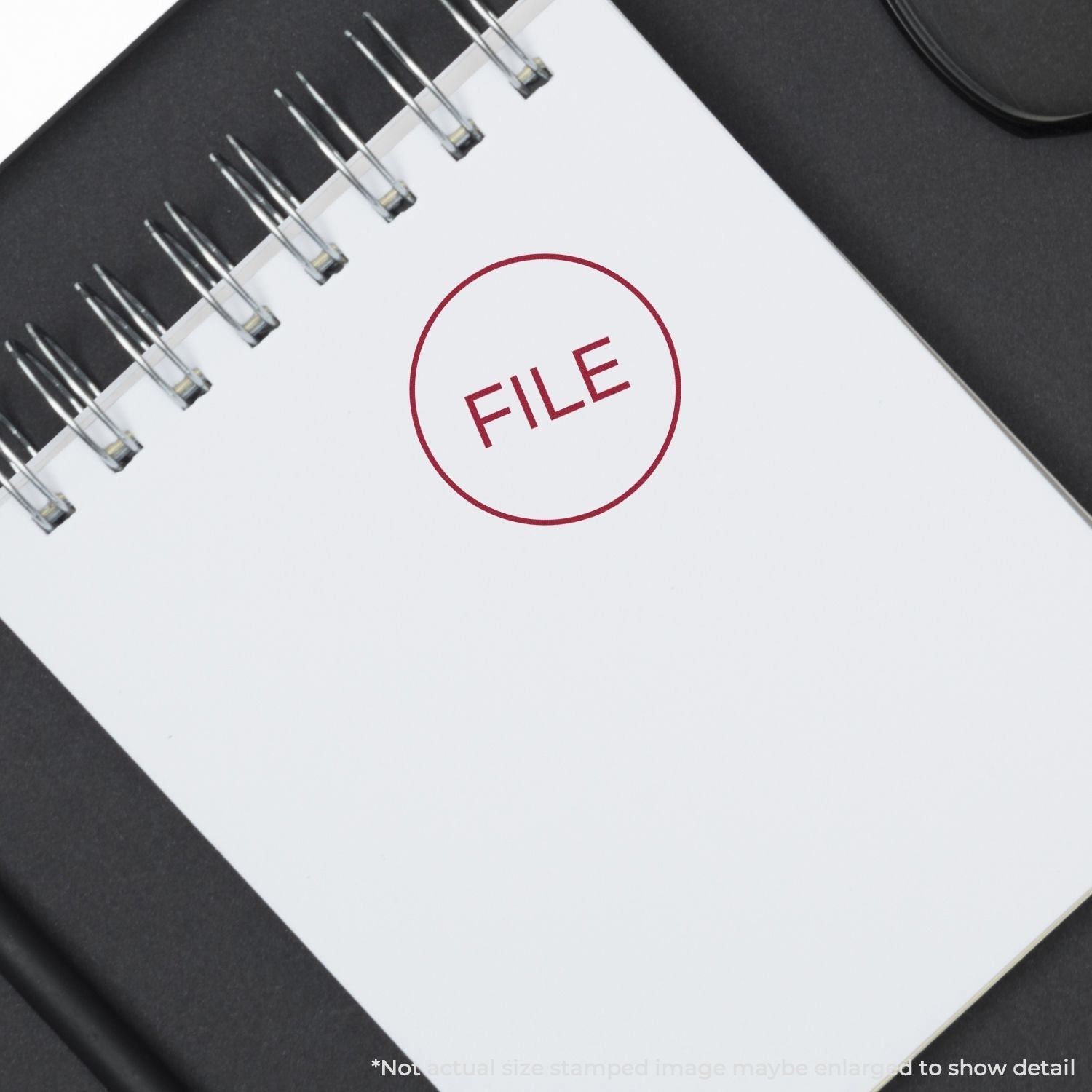 Self Inking Round File Stamp used on a white spiral notebook, leaving a clear red FILE mark in the center of the page.
