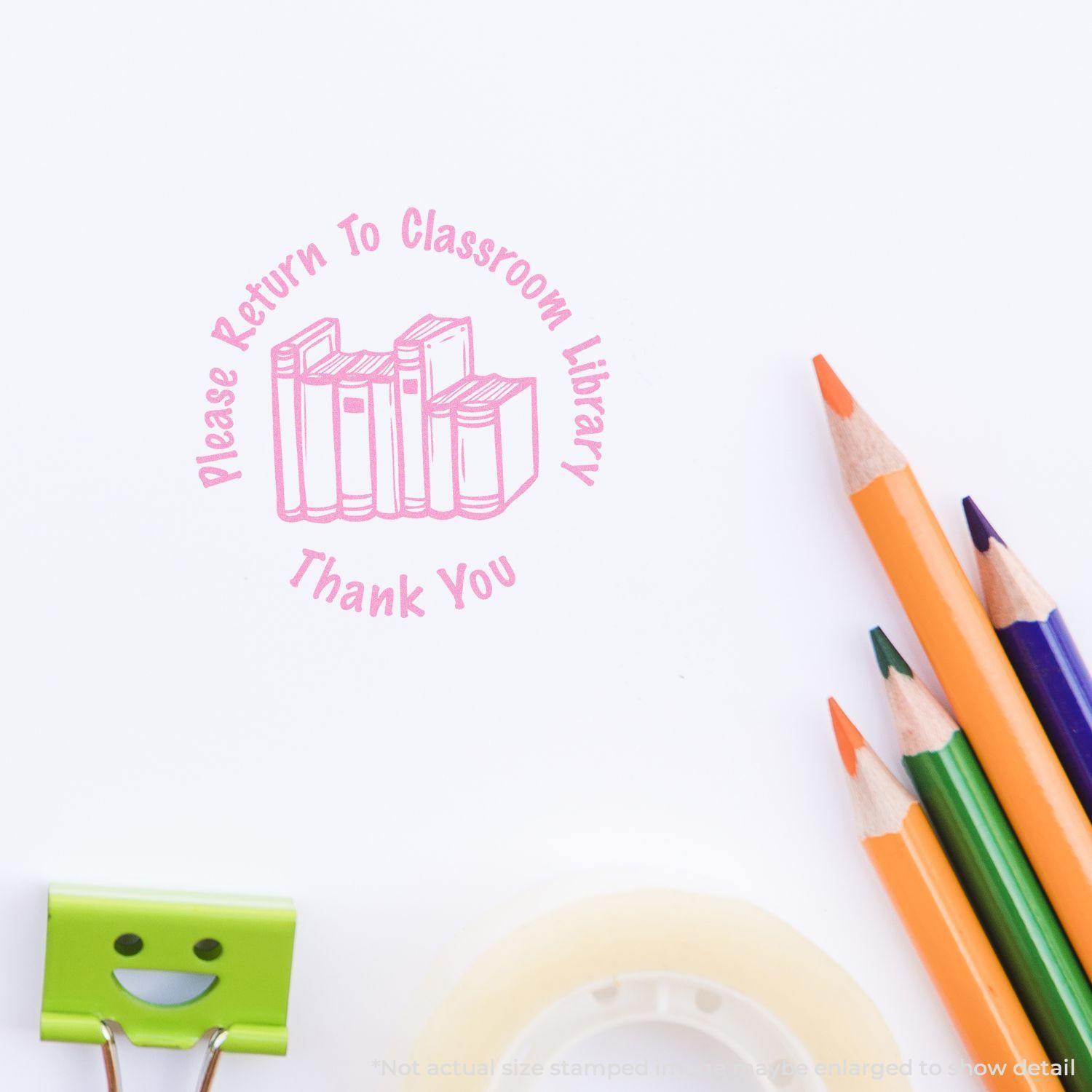 Round Please Return to Classroom Library rubber stamp in pink ink on white paper, with colored pencils and stationery nearby.