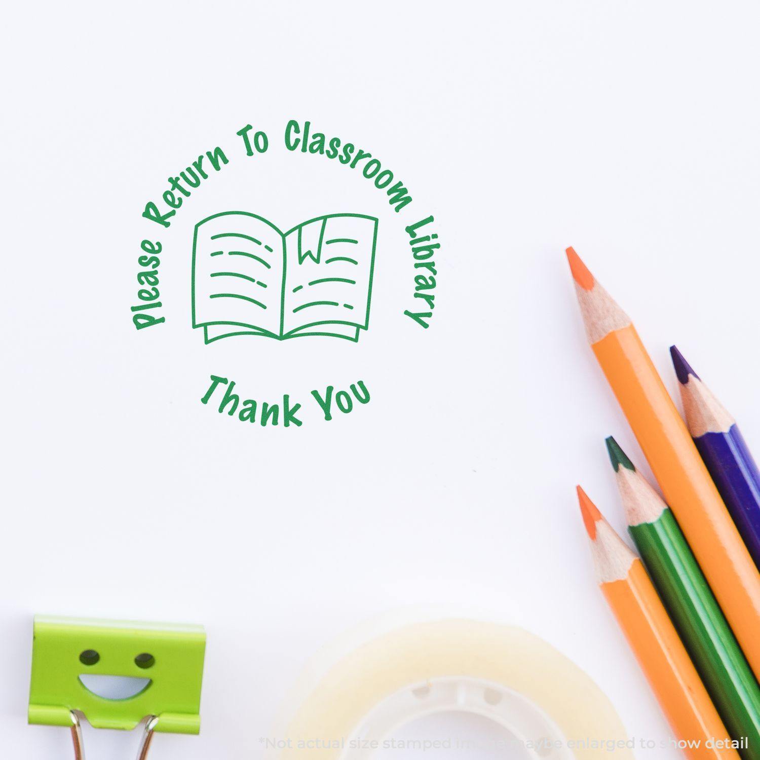 Round Please Return to Classroom Library rubber stamp impression with an open book icon, next to pencils and a smiley clip.