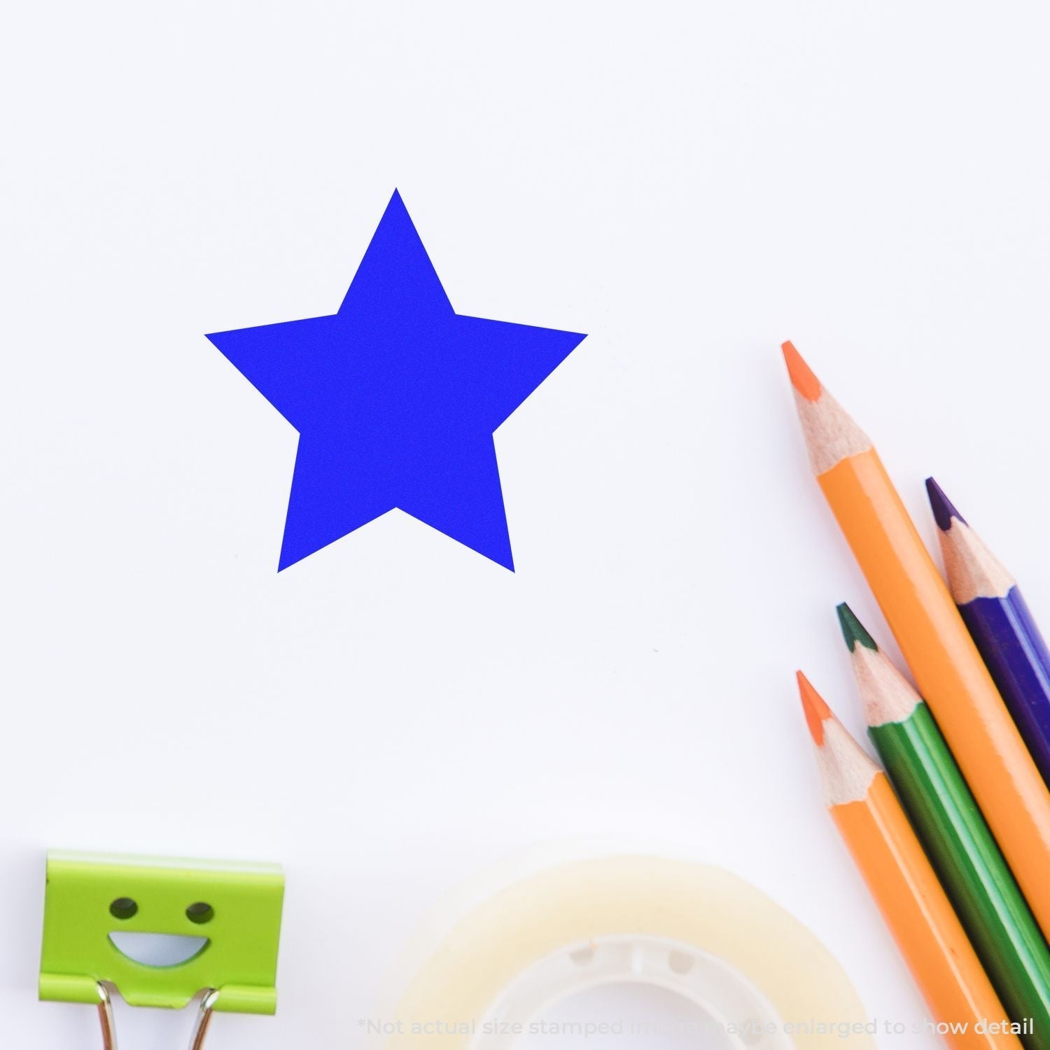 Self Inking Round Solid Star Stamp in blue on paper, surrounded by colorful pencils, a smiley face clip, and tape.