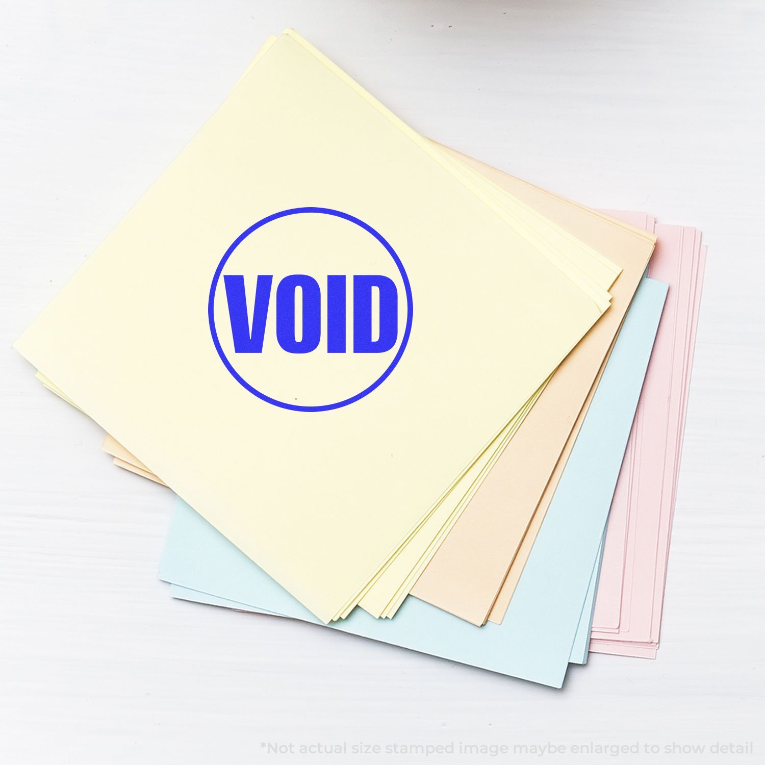 Self Inking Round Void Stamp marking VOID in blue on a stack of pastel-colored papers.