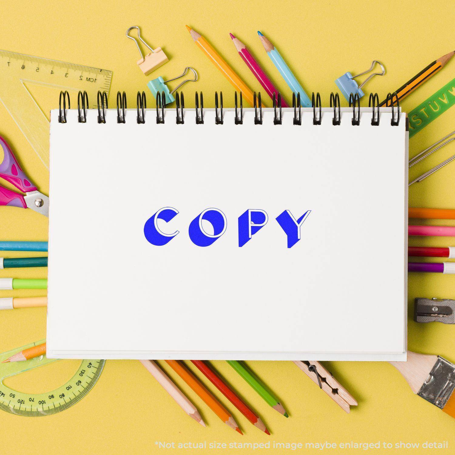 A notebook stamped with COPY using the Large Pre-Inked Shadow Copy Stamp, surrounded by colorful stationery on a yellow background.