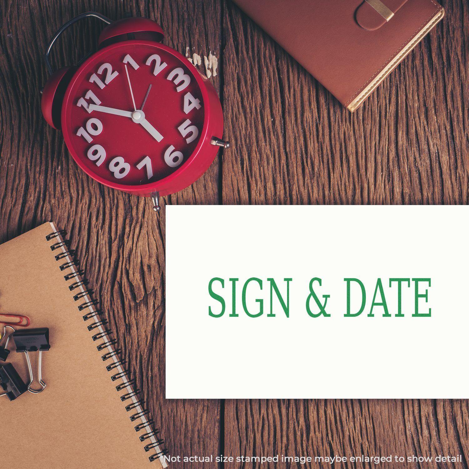 Large Sign & Date rubber stamp on a white card, placed on a wooden desk with a red clock, notebook, and office supplies.