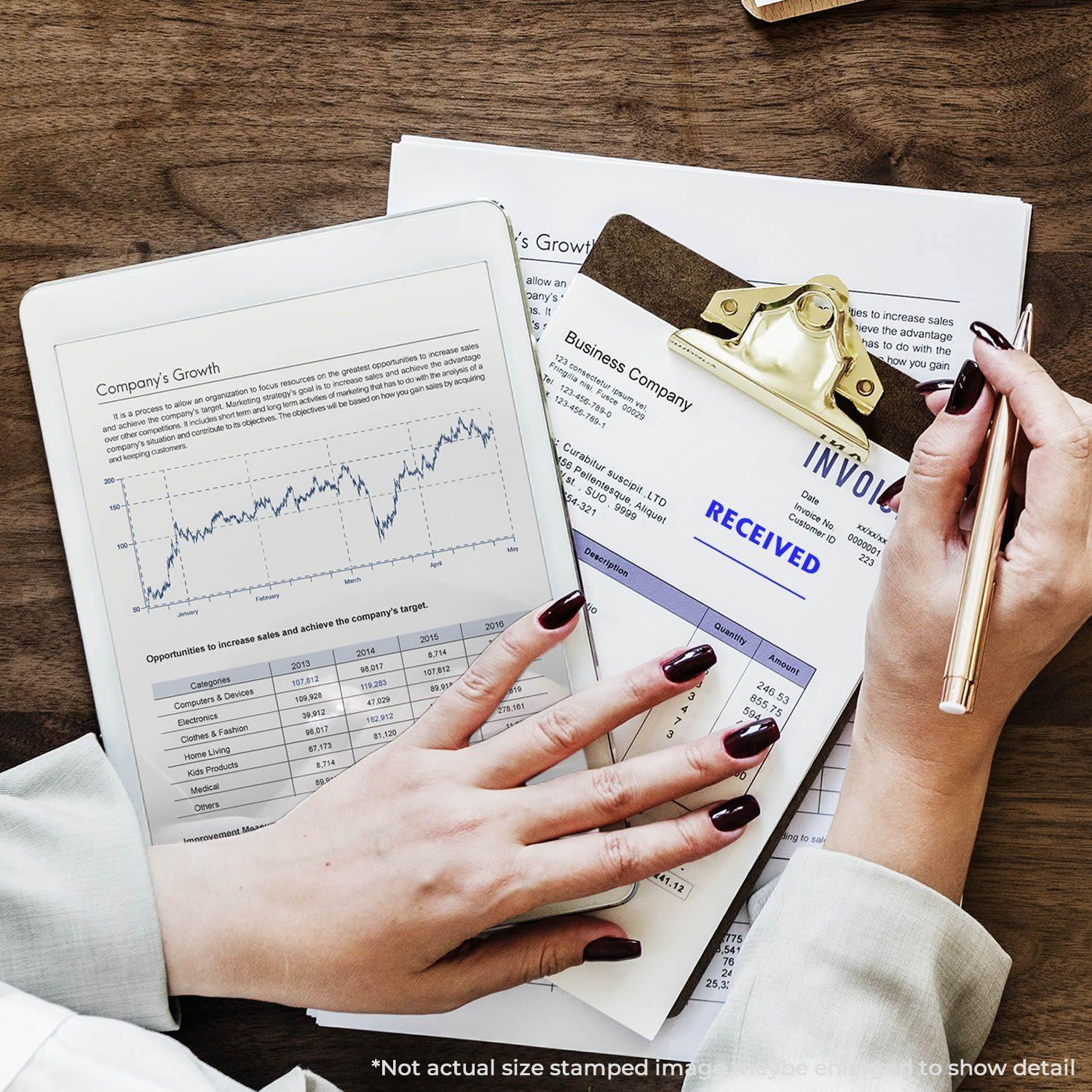Person using Slim Pre-Inked Received Stamp Two Lines on an invoice, with a tablet displaying a company growth chart nearby.