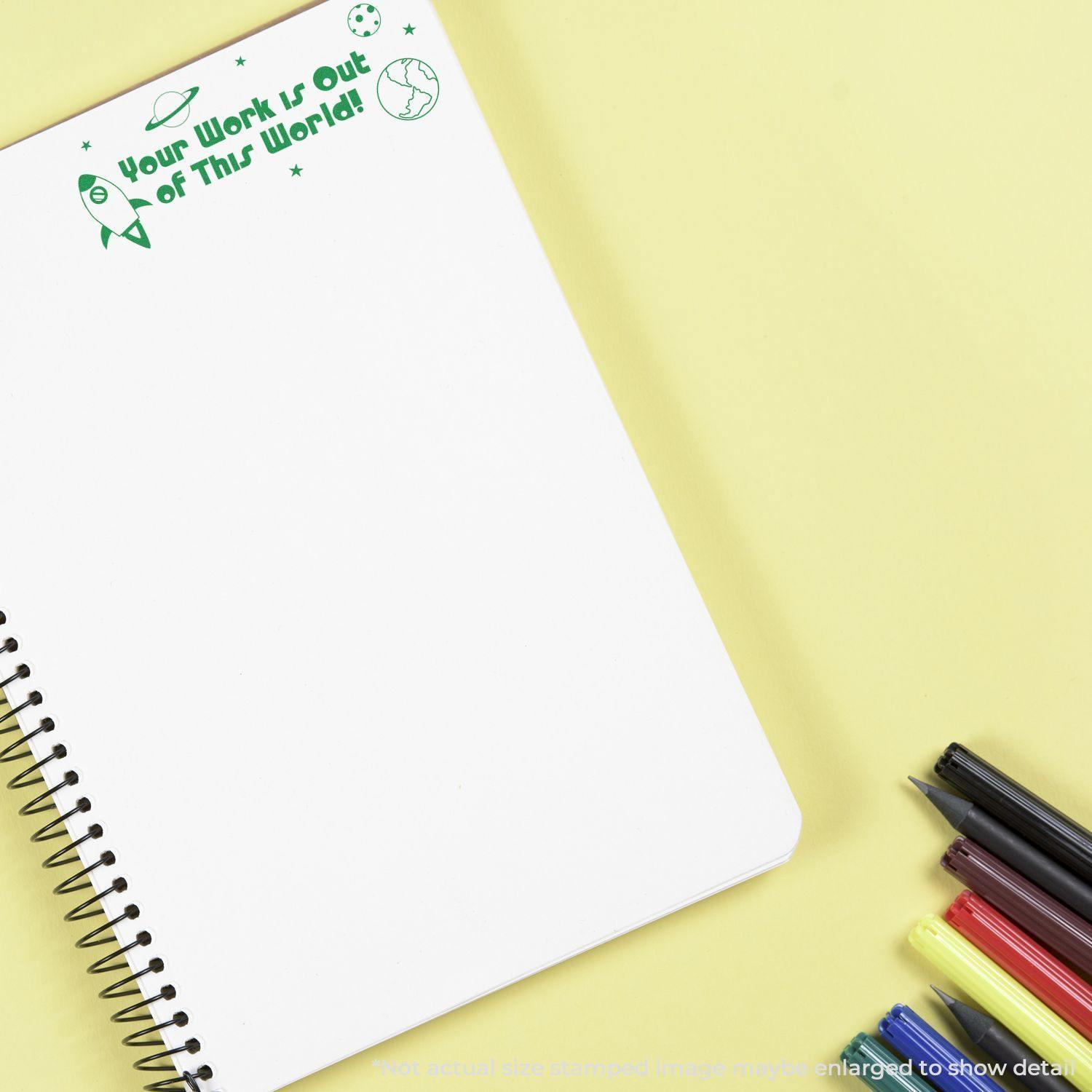 Large Self Inking Your Work is Out of this World Stamp used on a blank notebook page with pens on a yellow background.