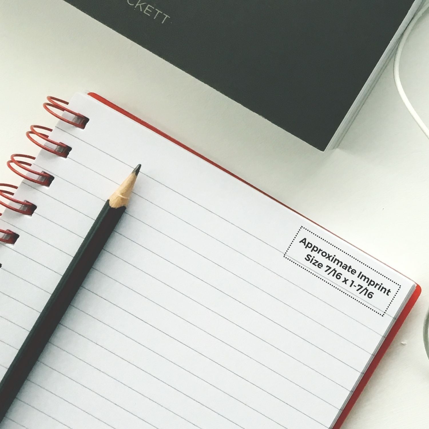 Super Slim 1442 Customized Pre-Inked Stamp 1/2 x 1-5/8 on a lined notebook with a pencil, showing the approximate imprint size.