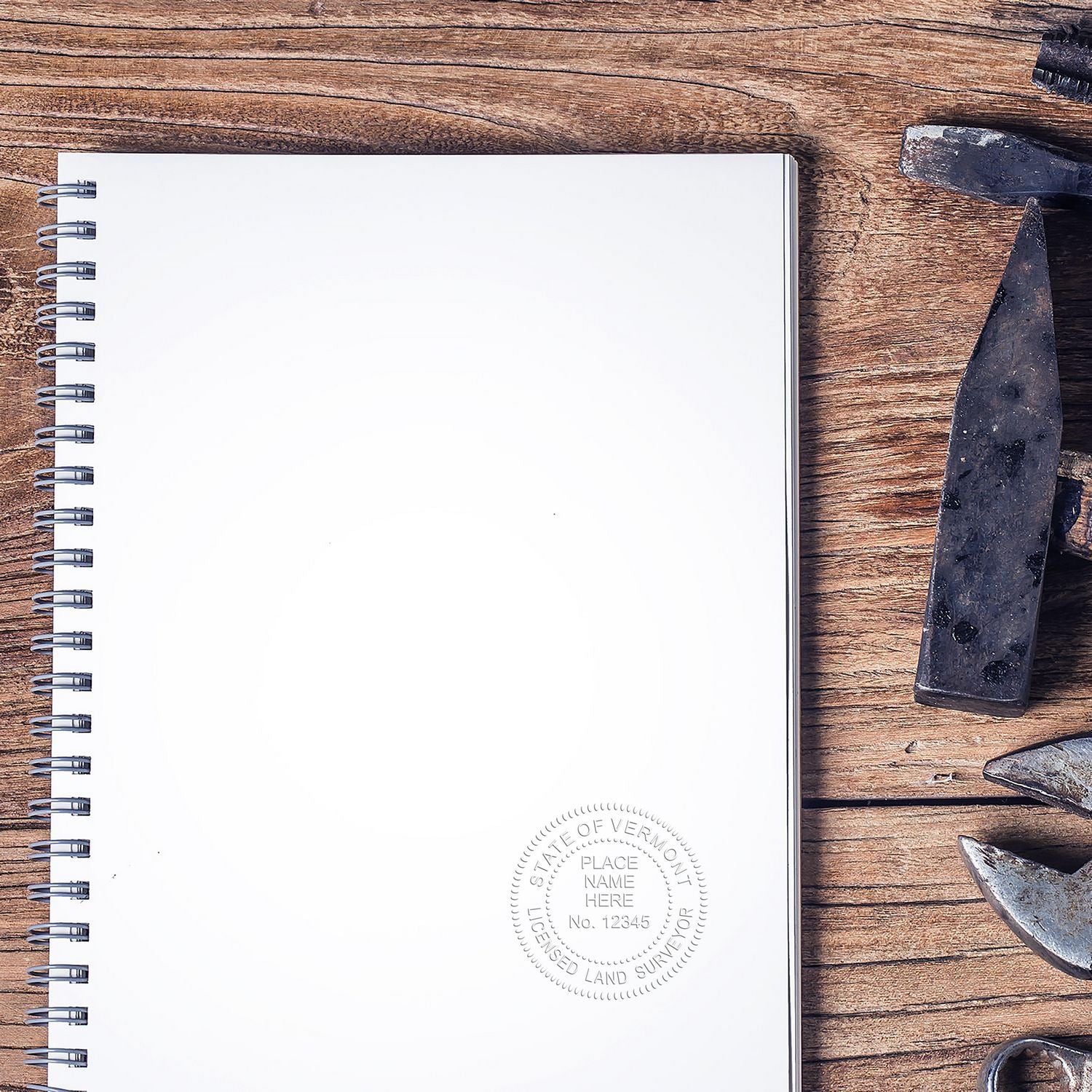 A Land Surveyor Gold Gift Seal Embosser imprint on a blank spiral notebook, surrounded by surveying tools on a wooden surface.