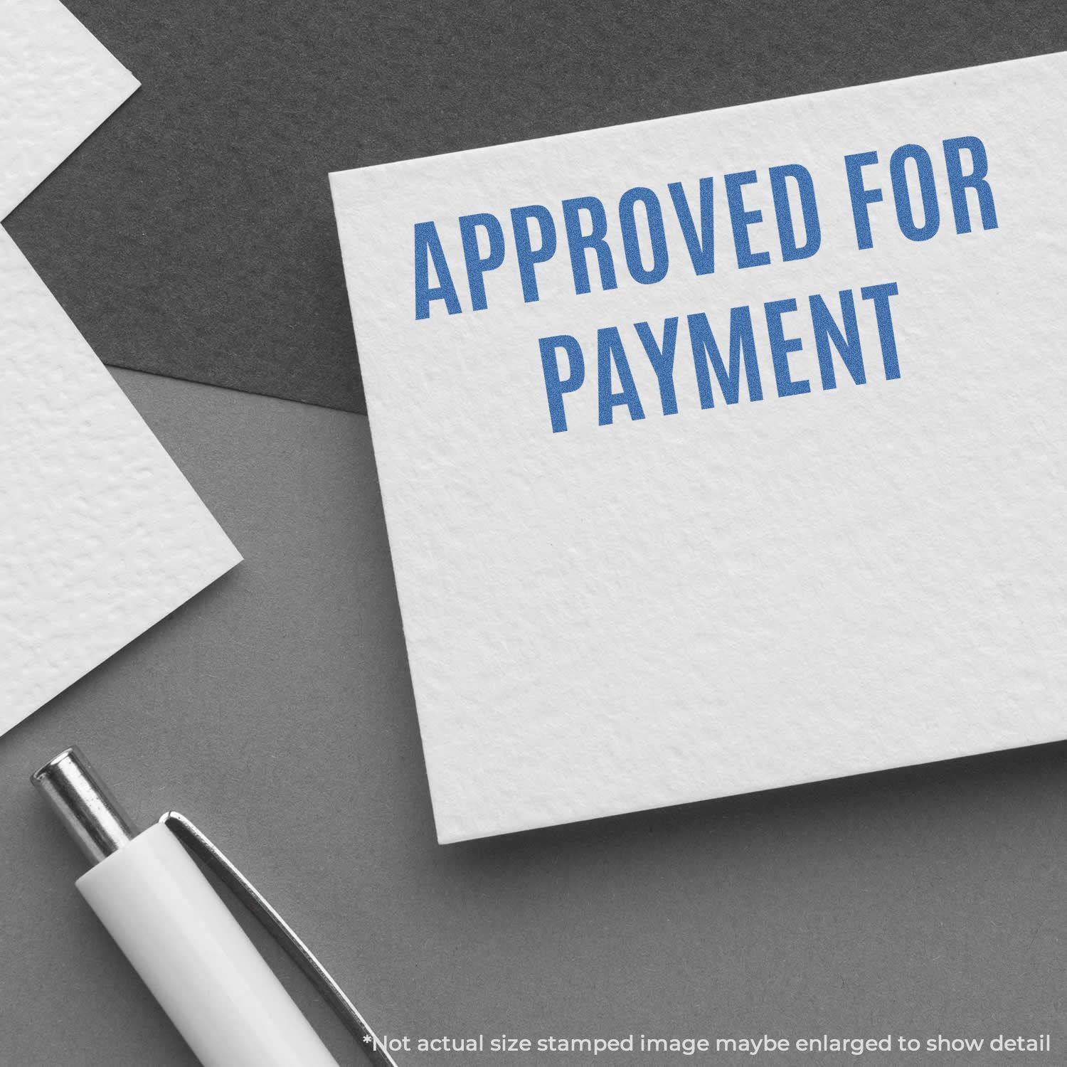 Approved For Payment Xstamper Stamp imprint on a white card, placed on a dark surface with a pen nearby.