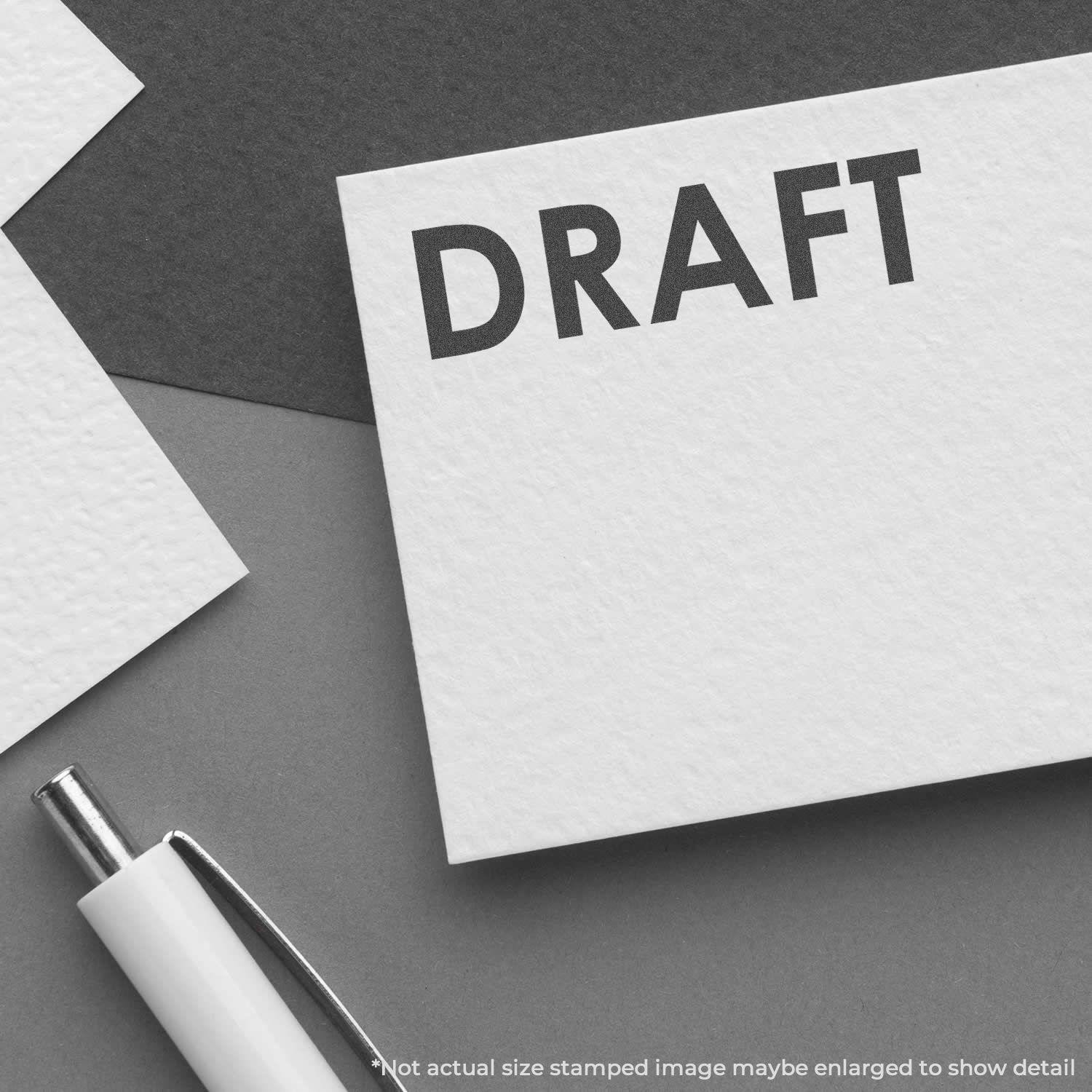 Black Draft Xstamper Stamp imprinting the word DRAFT on a white card, with a pen nearby on a dark surface.