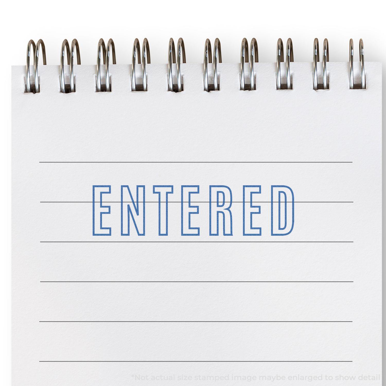 Blue Entered Xstamper Stamp imprint on a spiral-bound notebook with lined pages, showing the word ENTERED in blue ink.