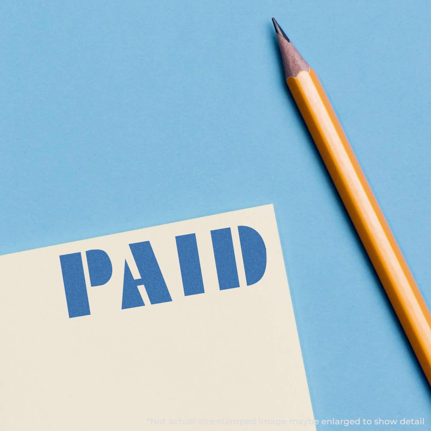 A Blue Paid Xstamper Stamp imprint on a paper next to a sharpened yellow pencil on a blue background.