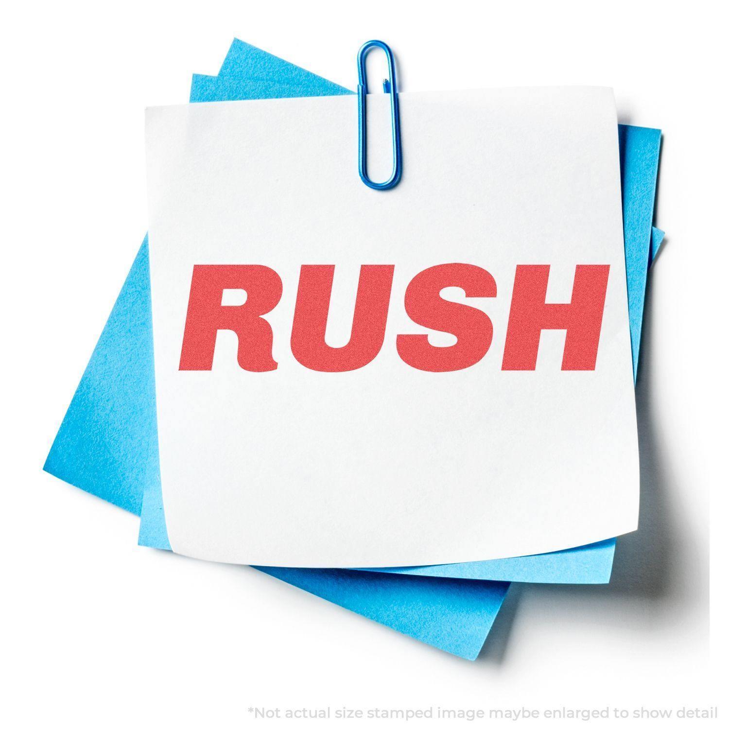 Bold Red Rush Xstamper Stamp imprint on white paper clipped to blue sheets, displaying the word RUSH in bold red letters.