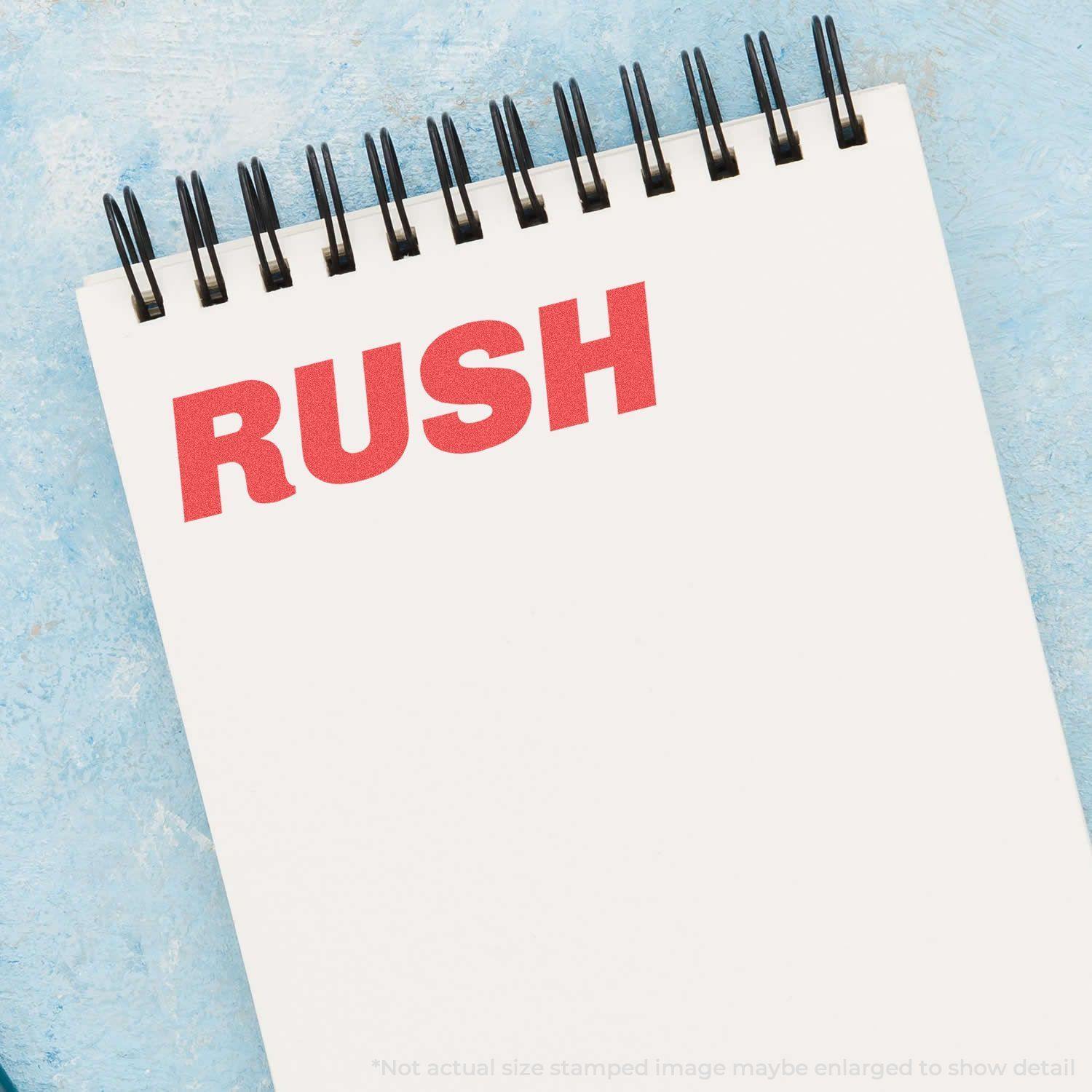 A notepad with RUSH stamped in bold red letters using the Bold Red Rush Xstamper Stamp, placed on a light blue surface.