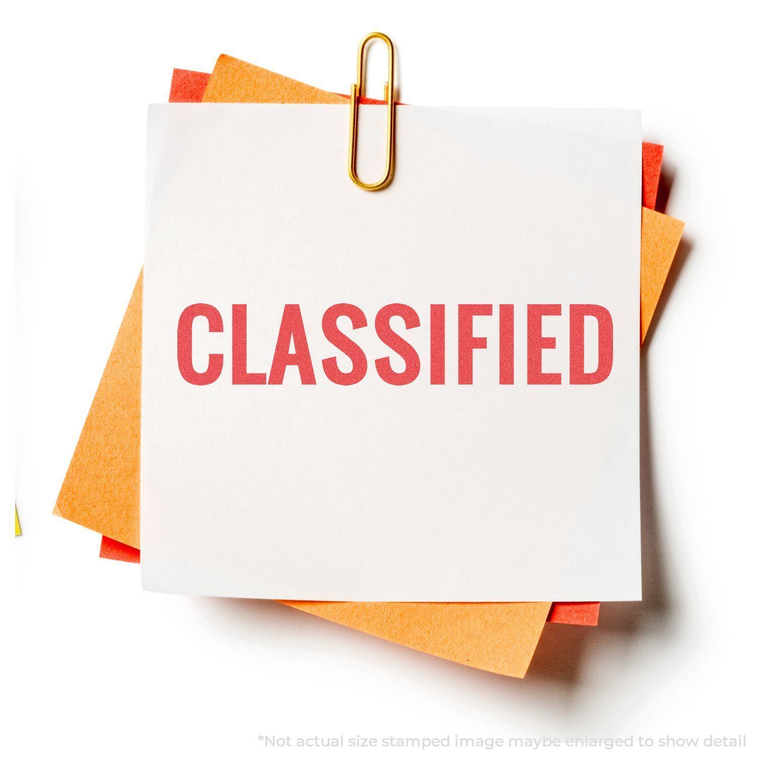 Classified Xstamper Stamp imprint on a white paper clipped to orange sheets, showing the word CLASSIFIED in bold red letters.