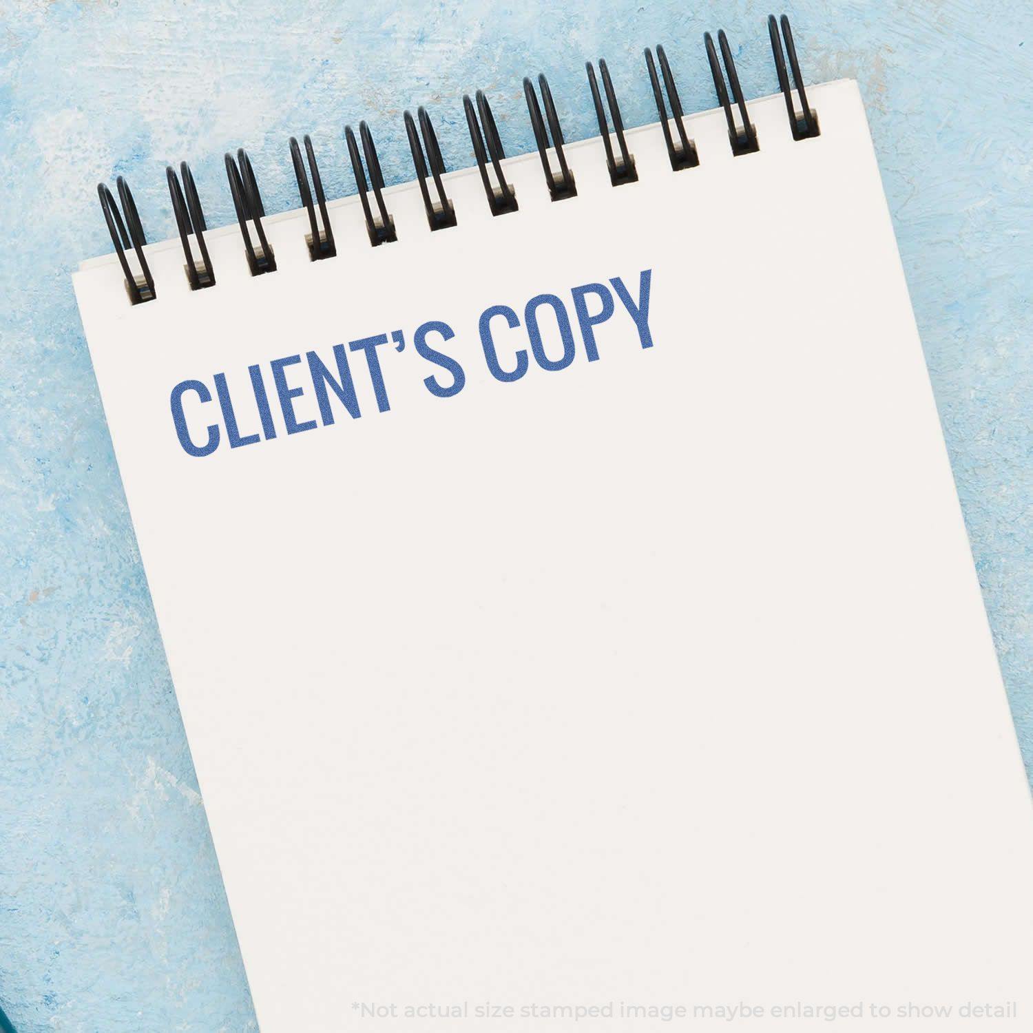A notepad with CLIENT'S COPY stamped in blue ink using the Client's Copy Xstamper Stamp, placed on a light blue surface.