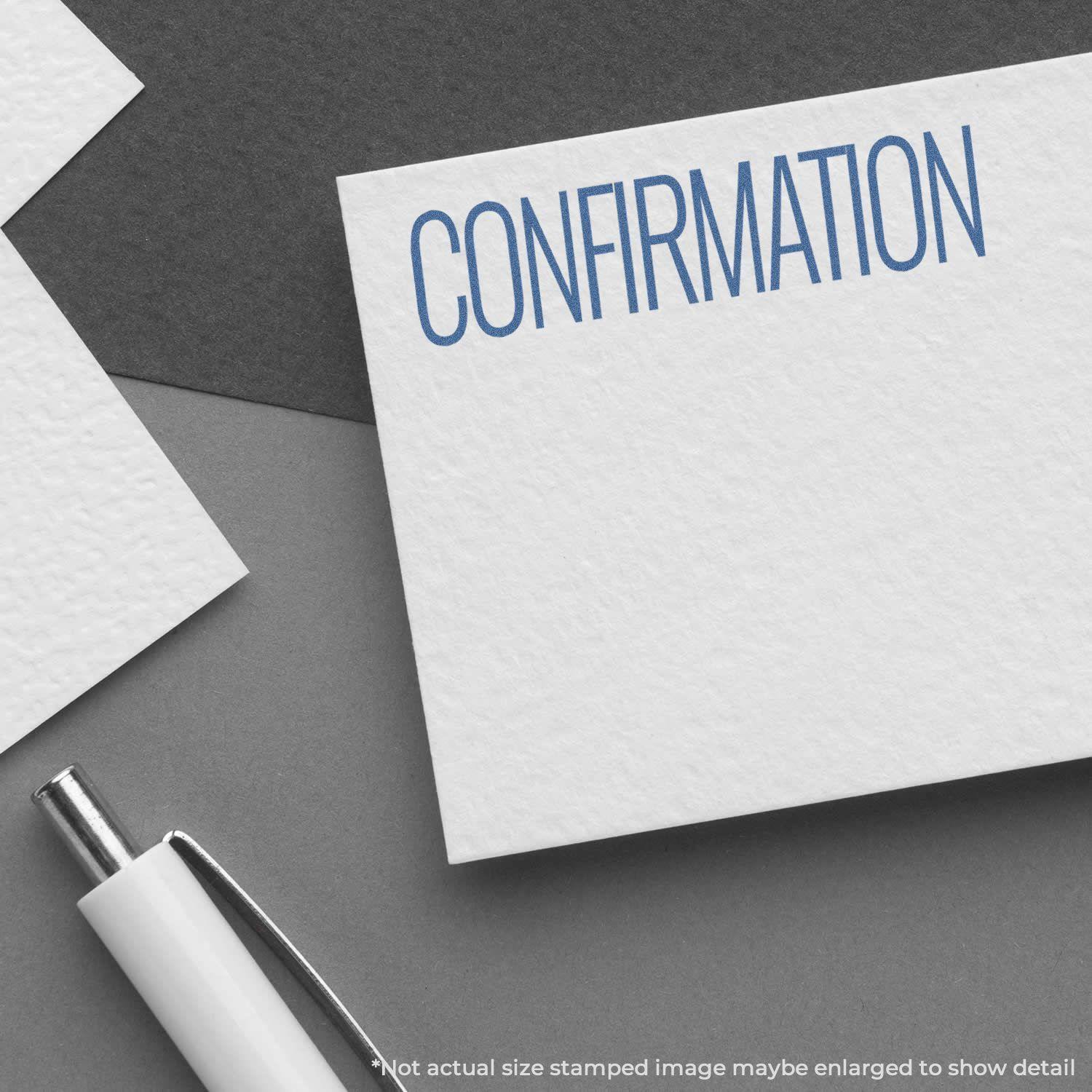 Confirmation Xstamper Stamp imprint on white paper, showing the word CONFIRMATION in blue ink, with a pen nearby on a gray surface.