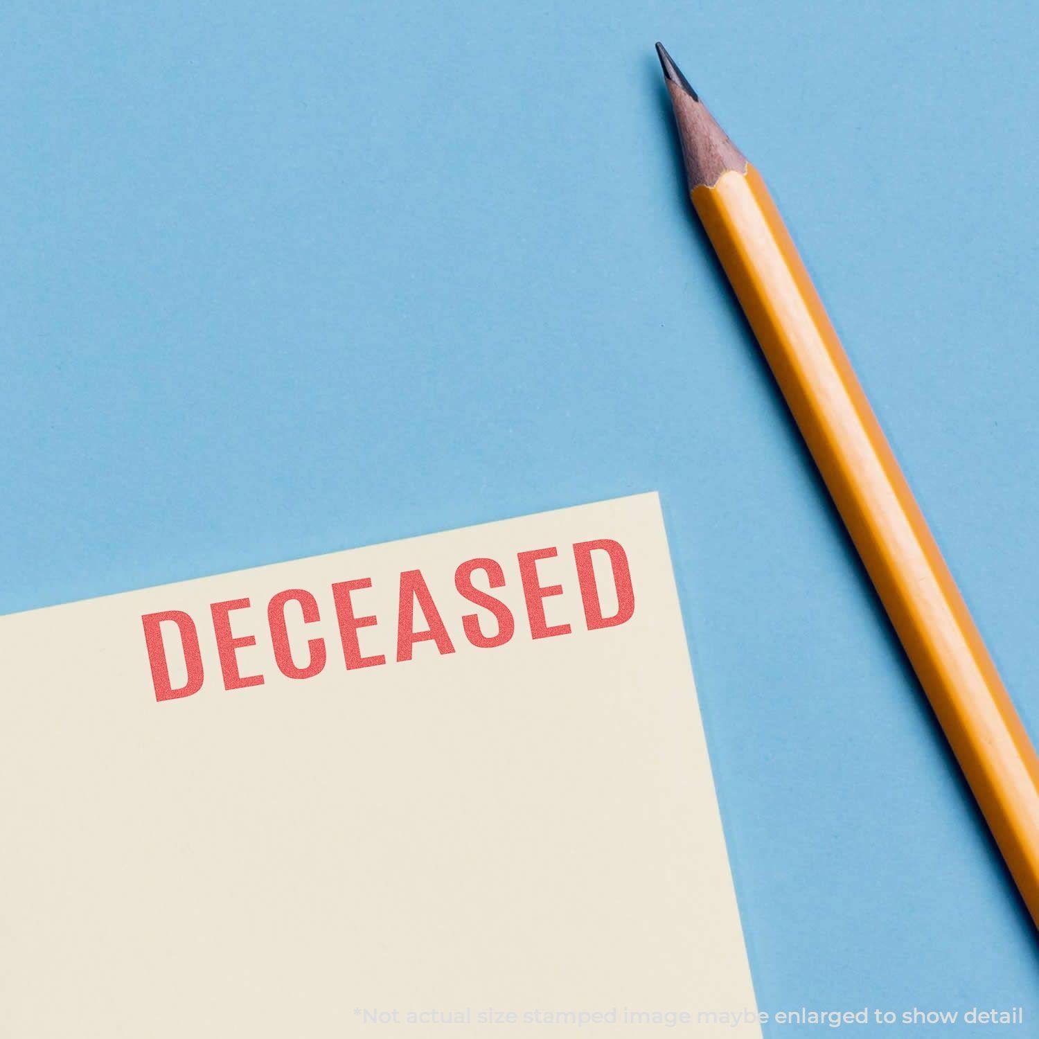 Deceased Xstamper Stamp in red ink on a yellow paper next to a sharpened yellow pencil on a blue background.
