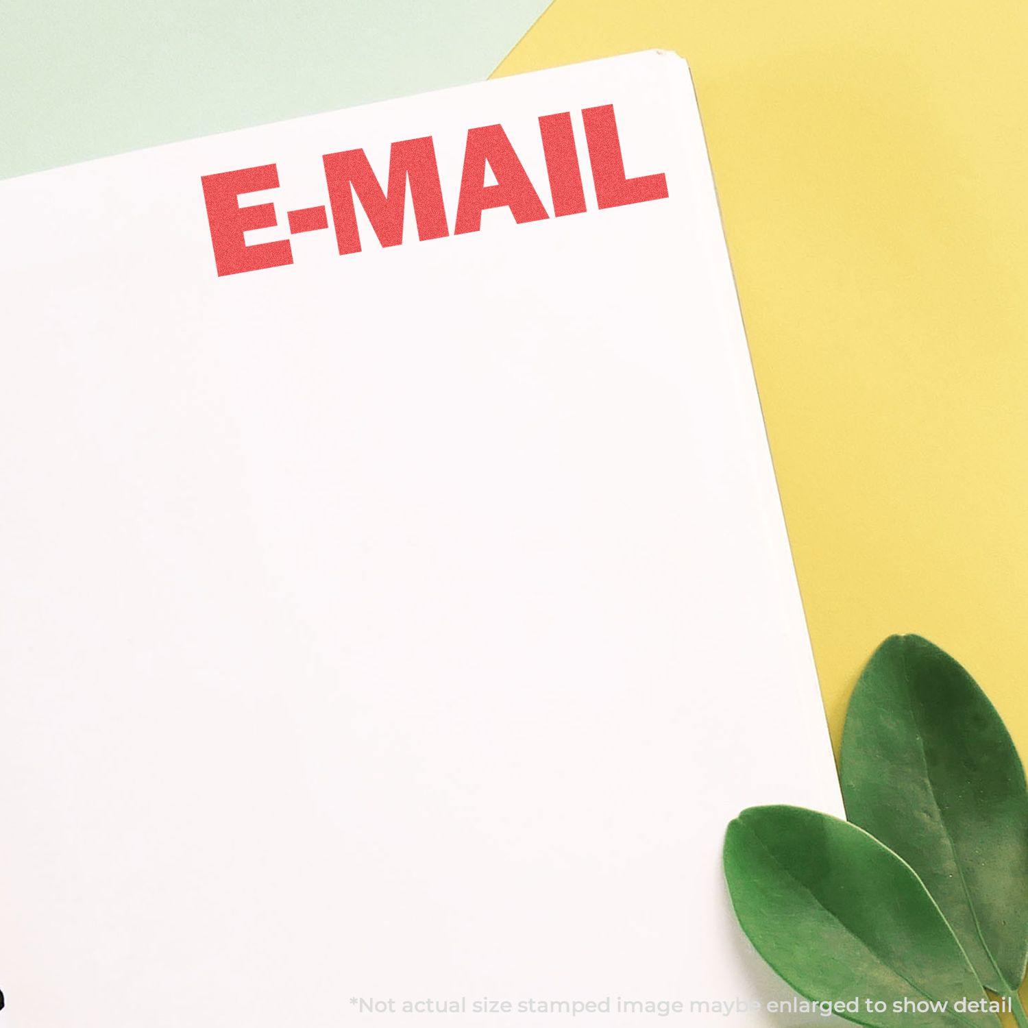 A white paper stamped with E-MAIL in red using the E-Mail Xstamper Stamp, placed on a yellow and green background with green leaves.