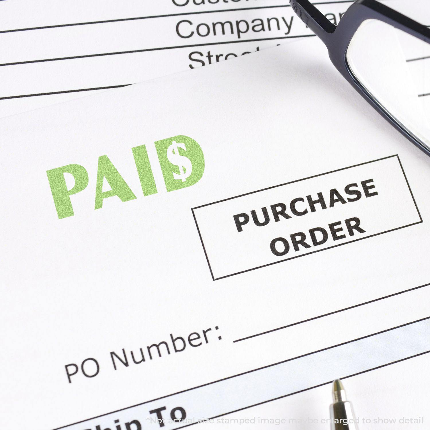 Green Paid Xstamper Stamp marking a purchase order with PAID in green ink, next to a pair of glasses and a pen.
