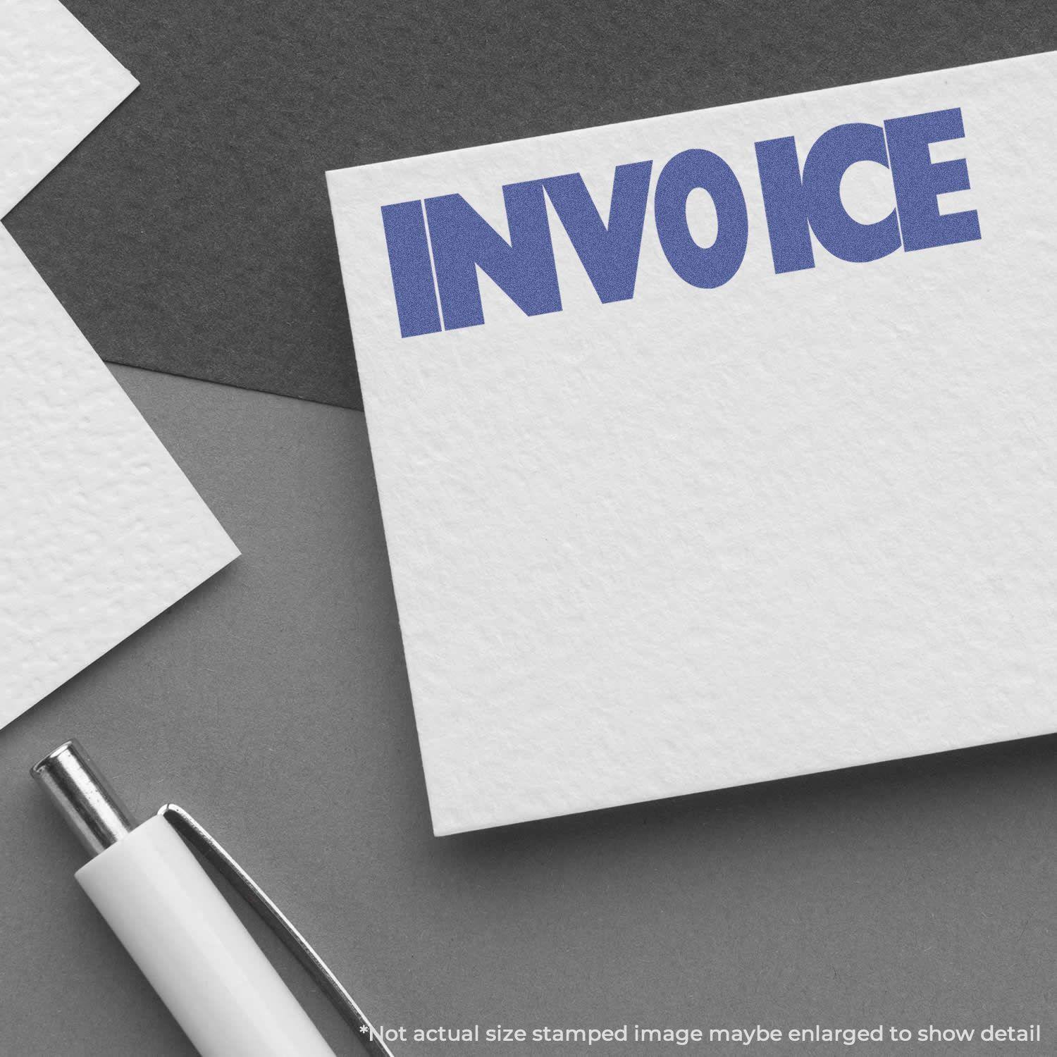 Invoice Xstamper Stamp imprinting INVOICE in blue on white paper, with a pen nearby.