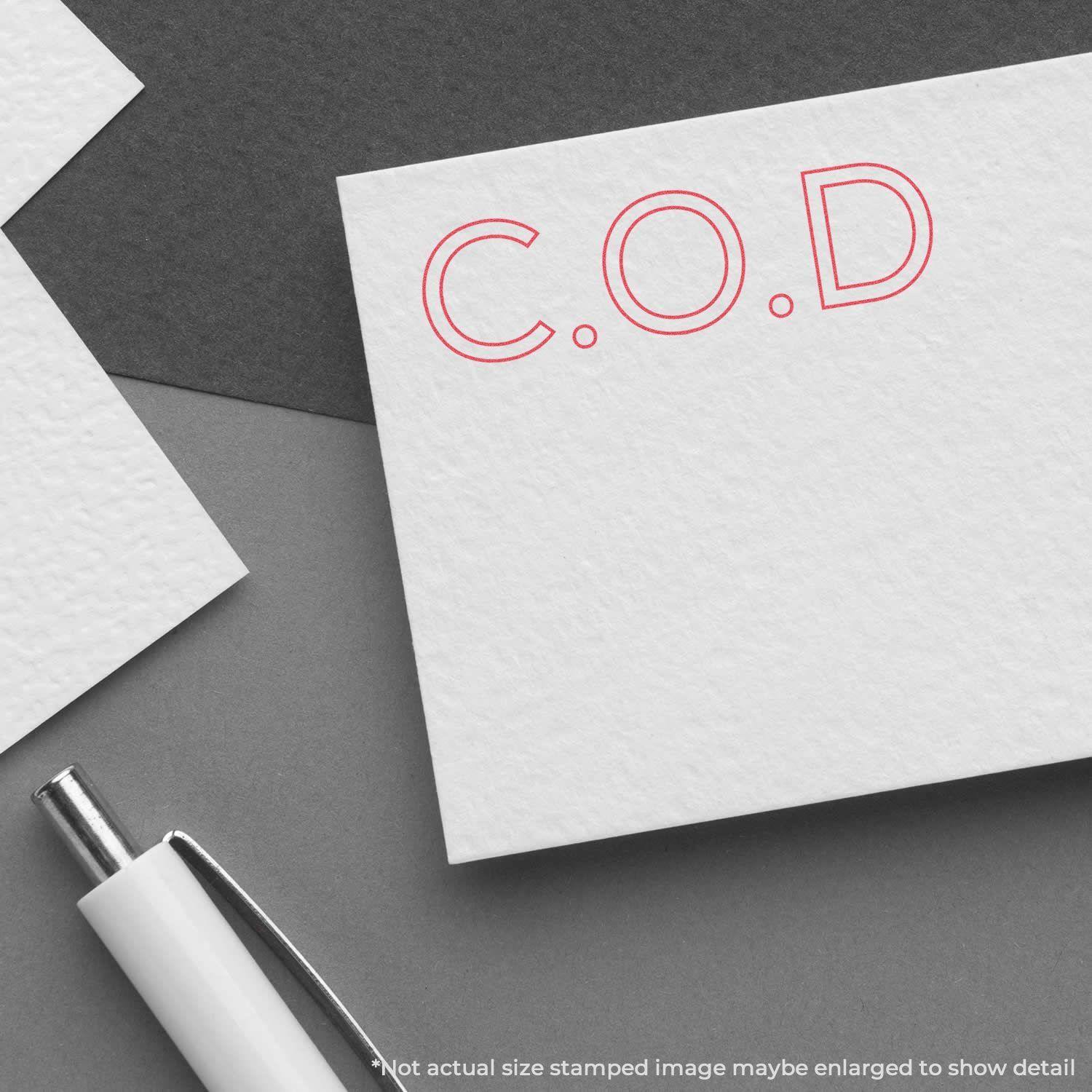Red C.O.D. Xstamper Stamp imprint on a white card, with a pen nearby on a gray background.