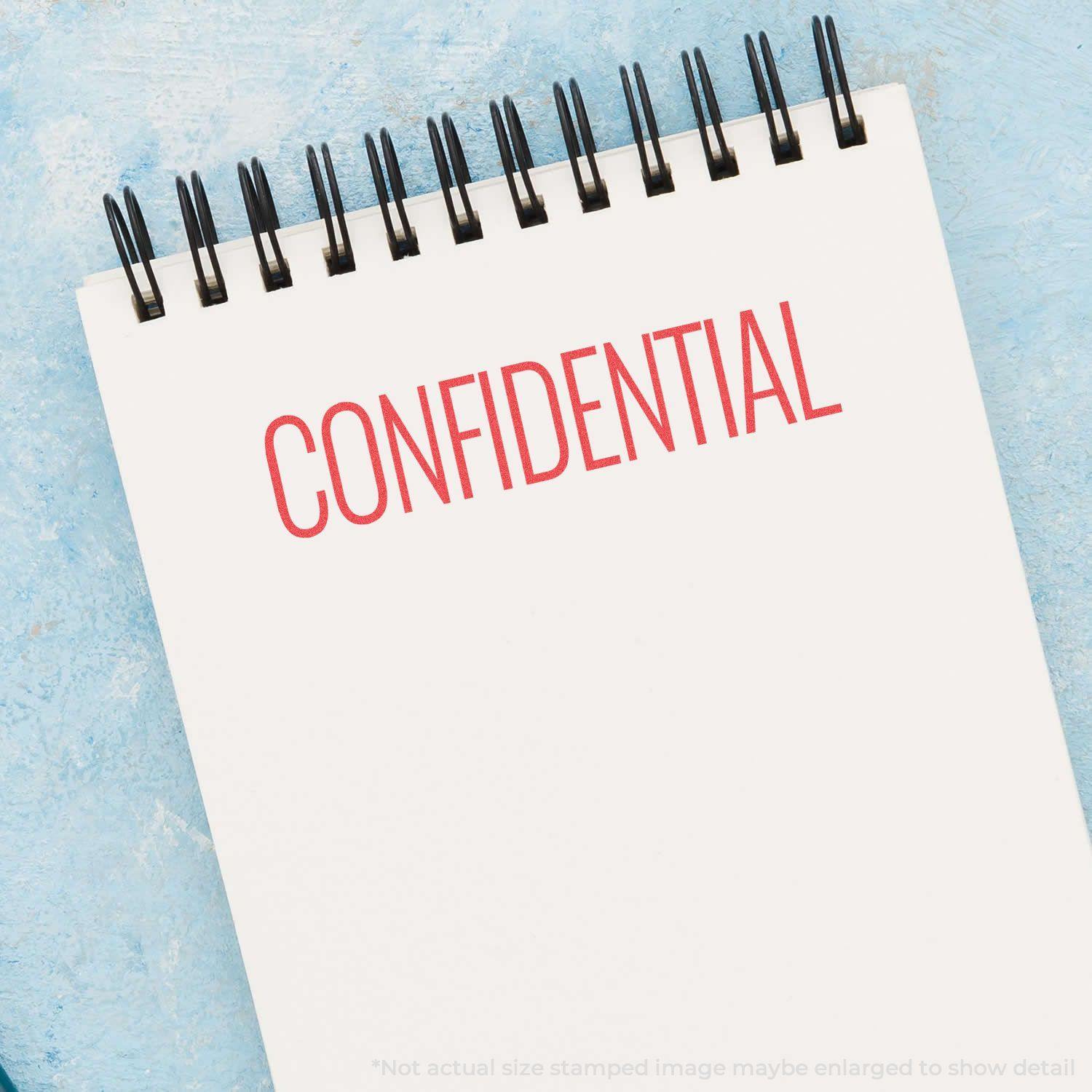 A notepad stamped with CONFIDENTIAL in red ink using the Red Confidential Xstamper Stamp, placed on a light blue surface.
