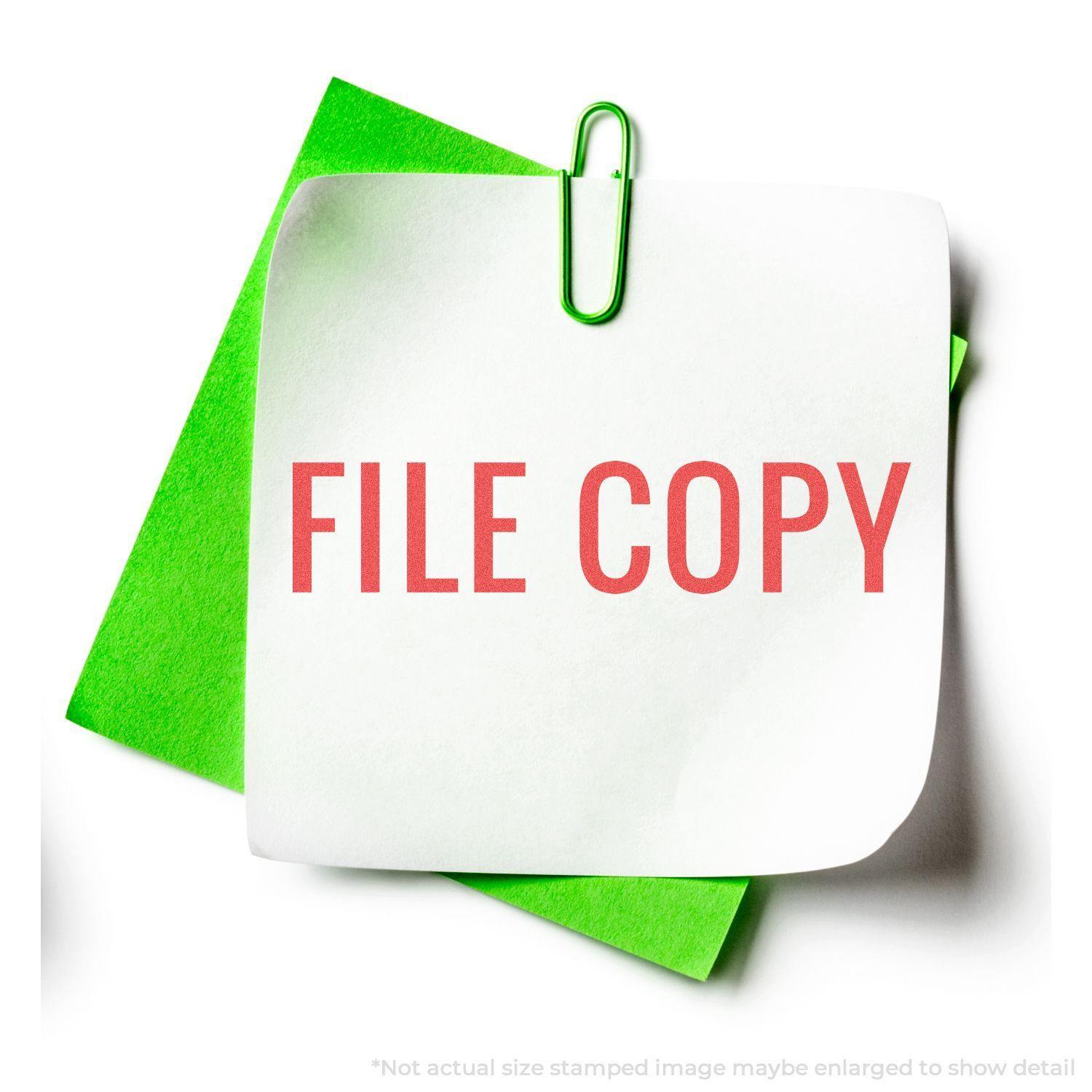Red File Copy Xstamper Stamp imprint on white paper with green paperclip and green background paper.