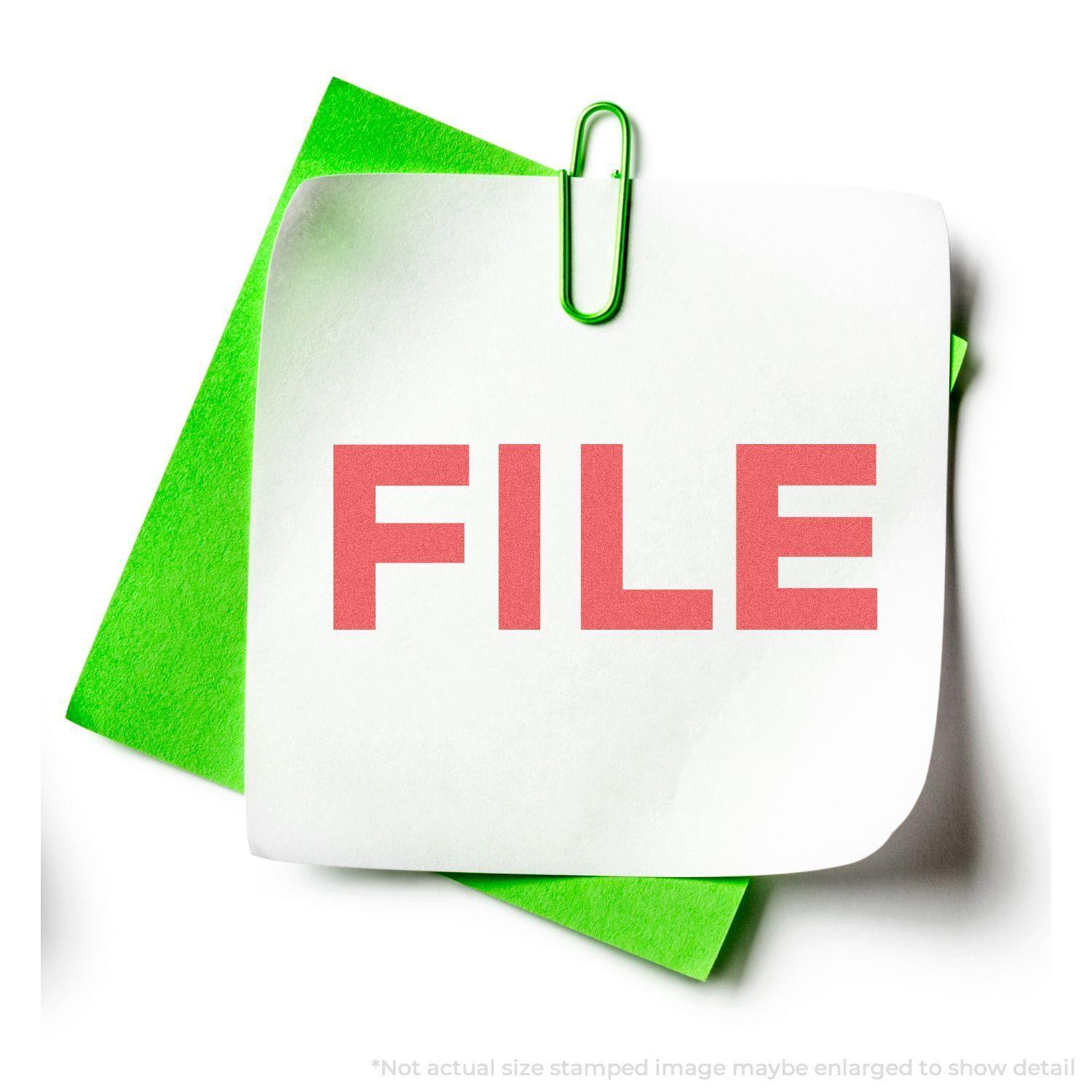 Red File Xstamper Stamp imprint on white paper clipped to a green folder. The word FILE is stamped in bold red letters.