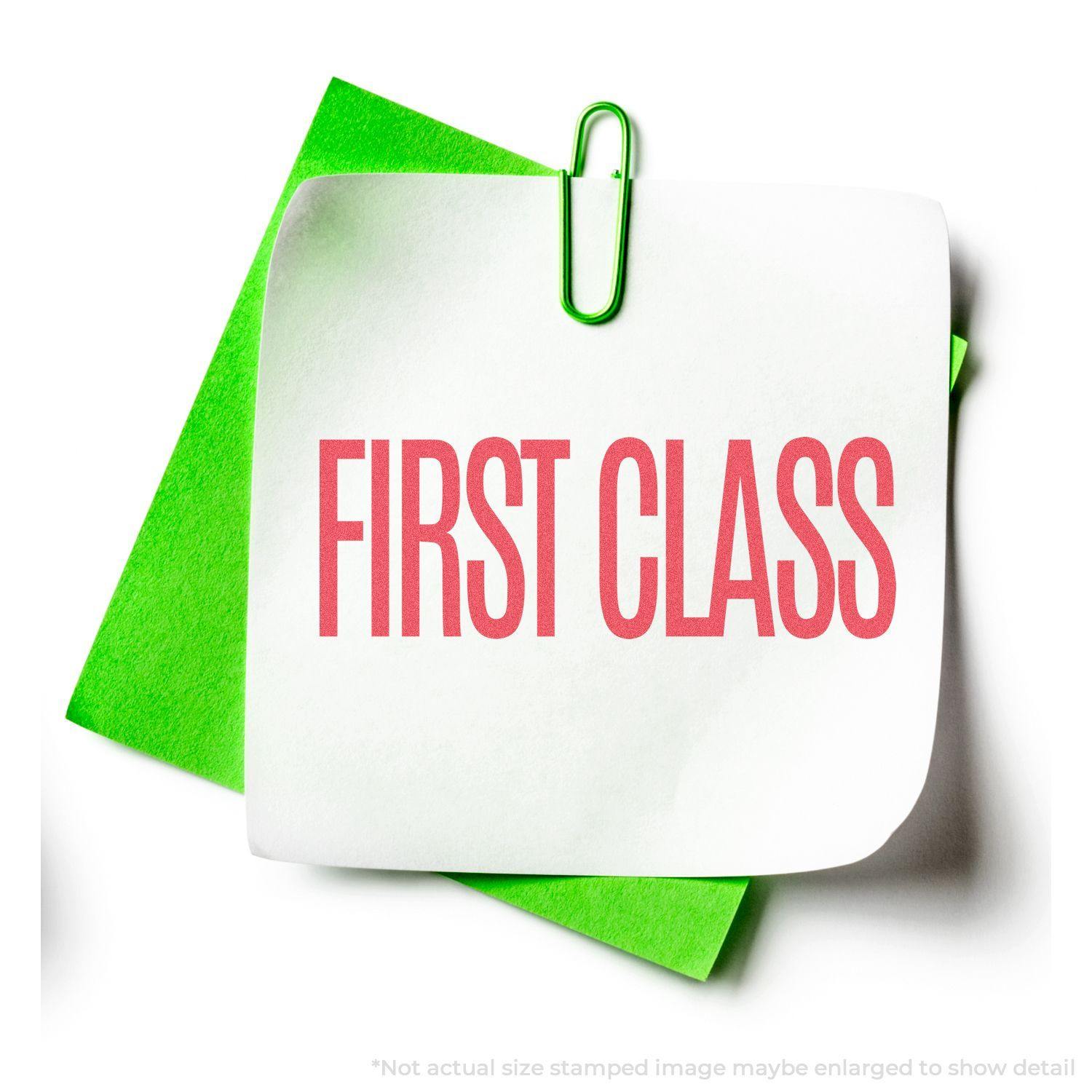 Red First Class Xstamper Stamp imprint on white paper, clipped to green paper with a green paperclip.