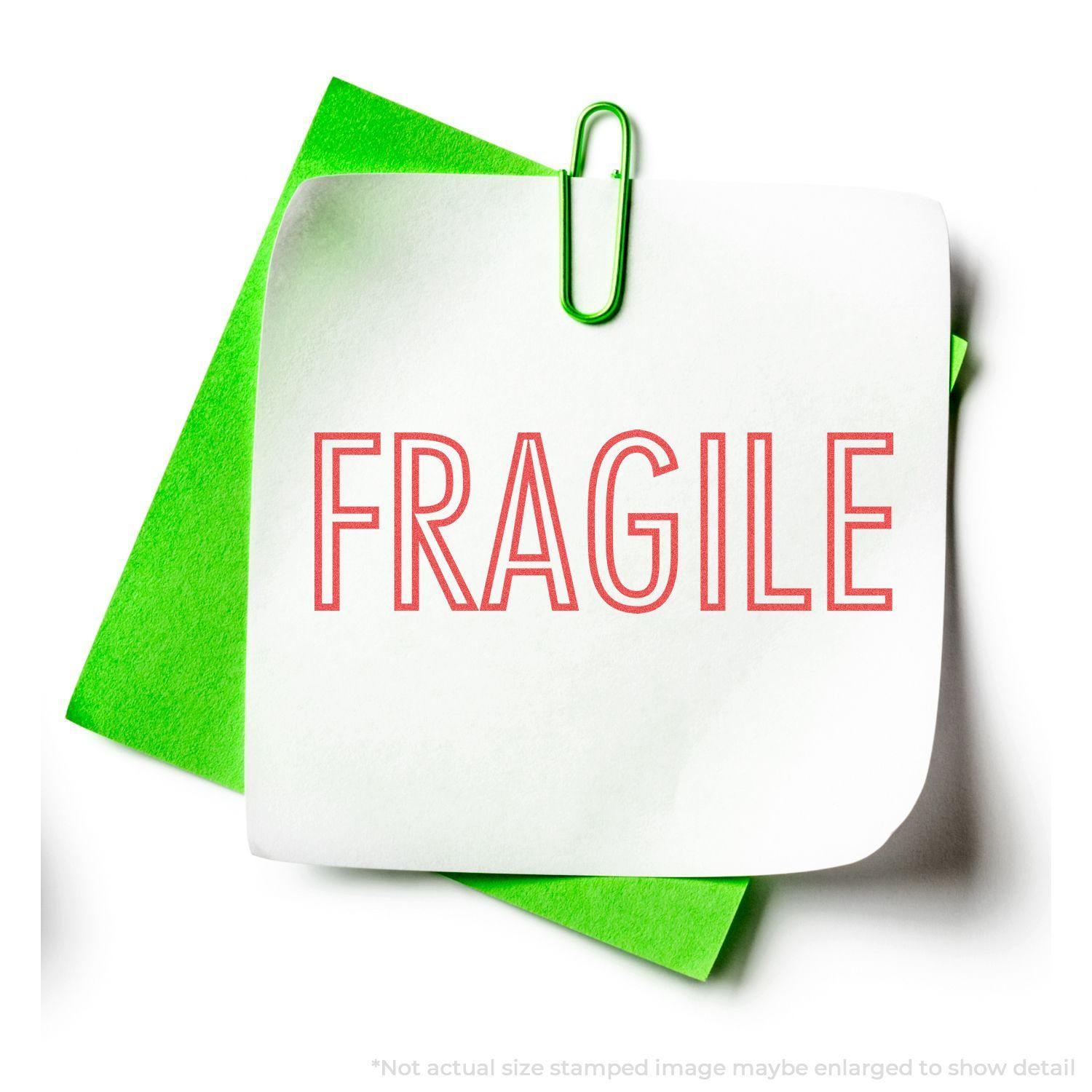 Red Fragile Xstamper Stamp imprint on white paper with green background and paperclip, indicating the item is fragile.