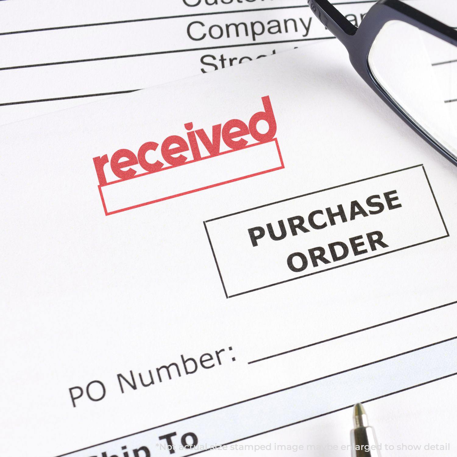 A purchase order stamped with the Red Received Xstamper Stamp, next to a pen and glasses on a desk.
