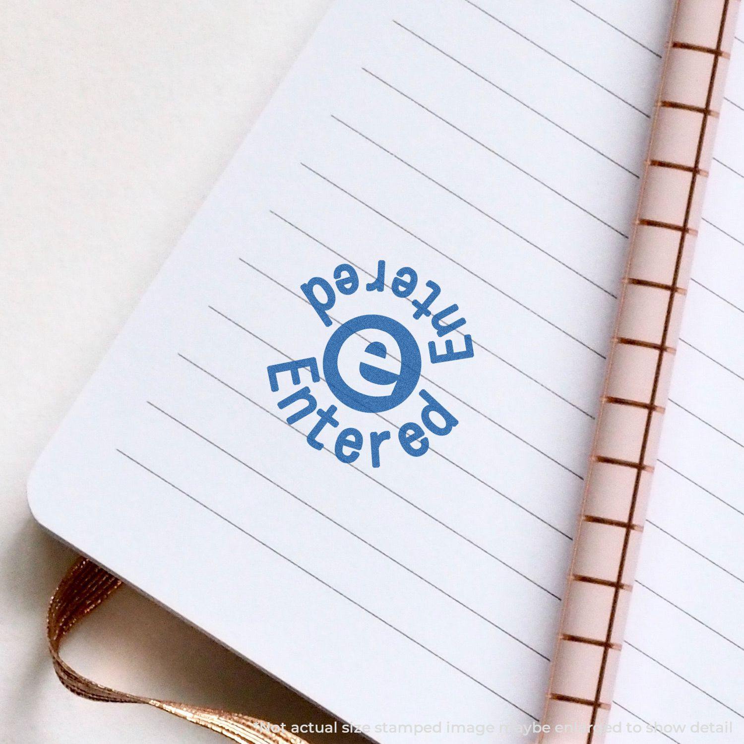 Round Blue Entered Xstamper Stamp imprint on a lined notebook page, showing clear and crisp Entered text in blue ink.