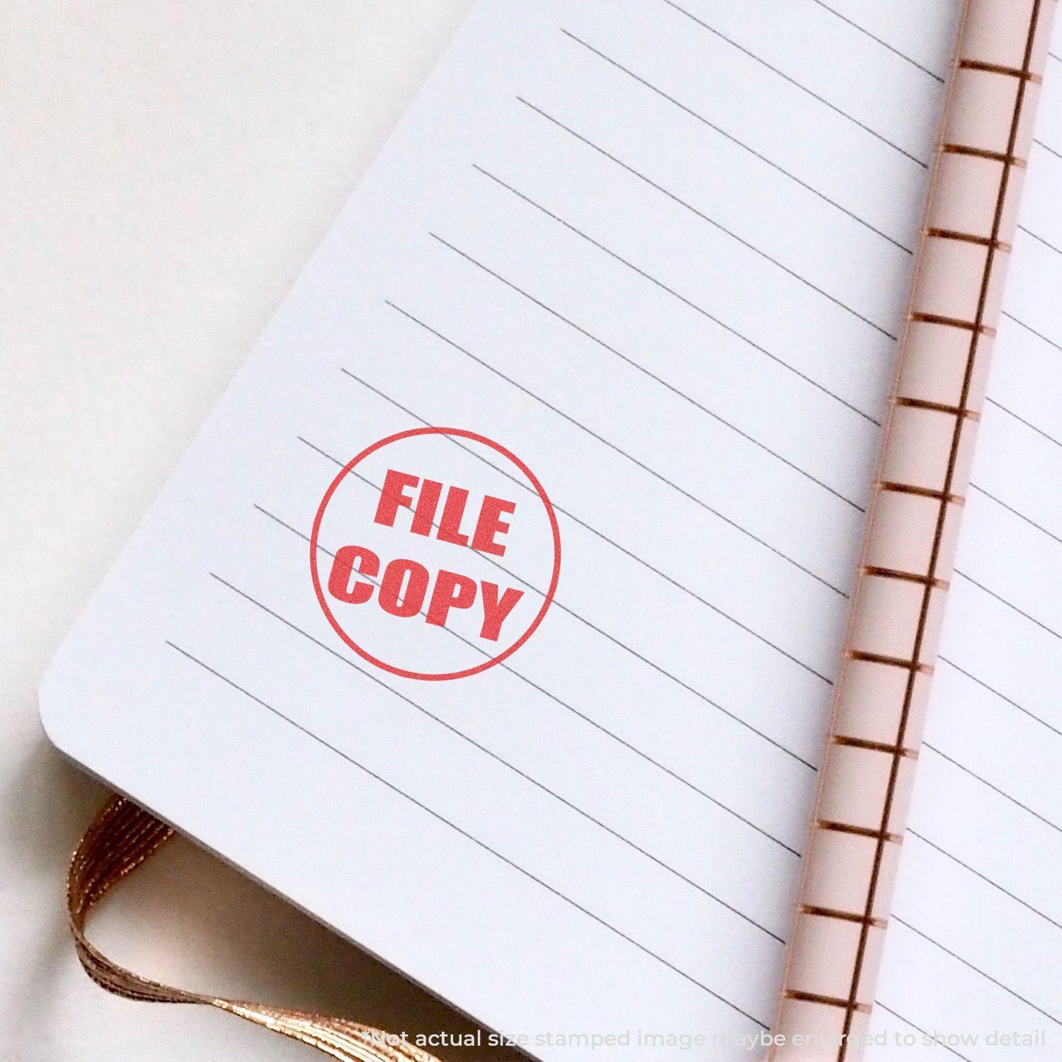 Round File Copy Xstamper Stamp imprinting FILE COPY in red on a lined notebook page with a spiral binding.