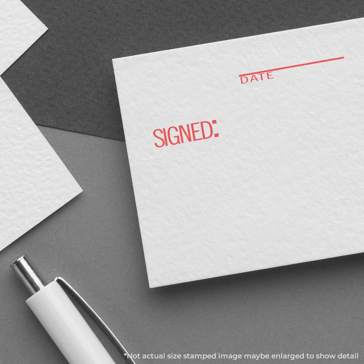 A Signed: Date Xstamper Stamp imprint in red ink on white paper, with a pen nearby on a gray background.