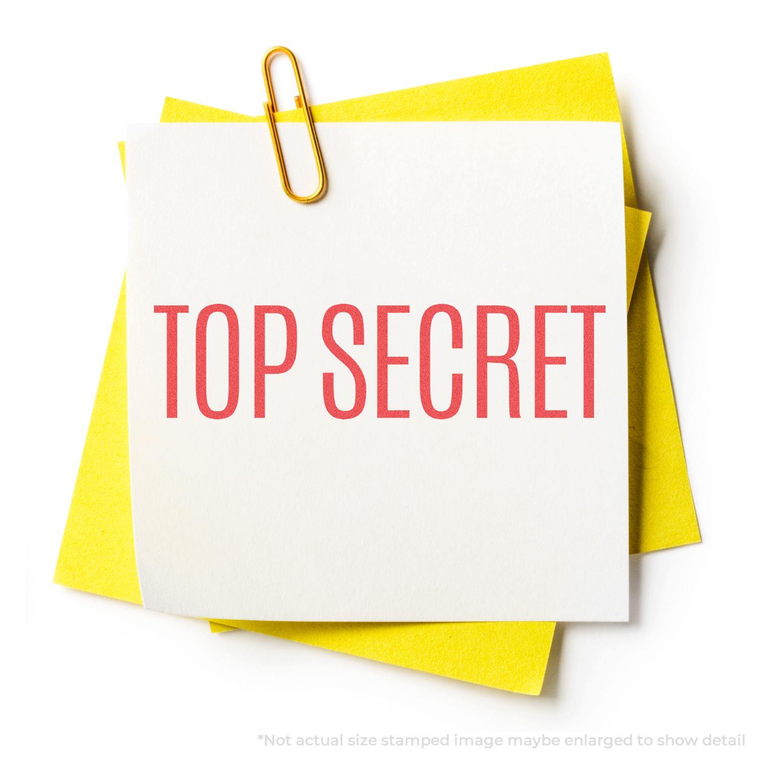 A Top Secret Xstamper Stamp imprint on a white note with a yellow paper underneath, held by a paperclip.