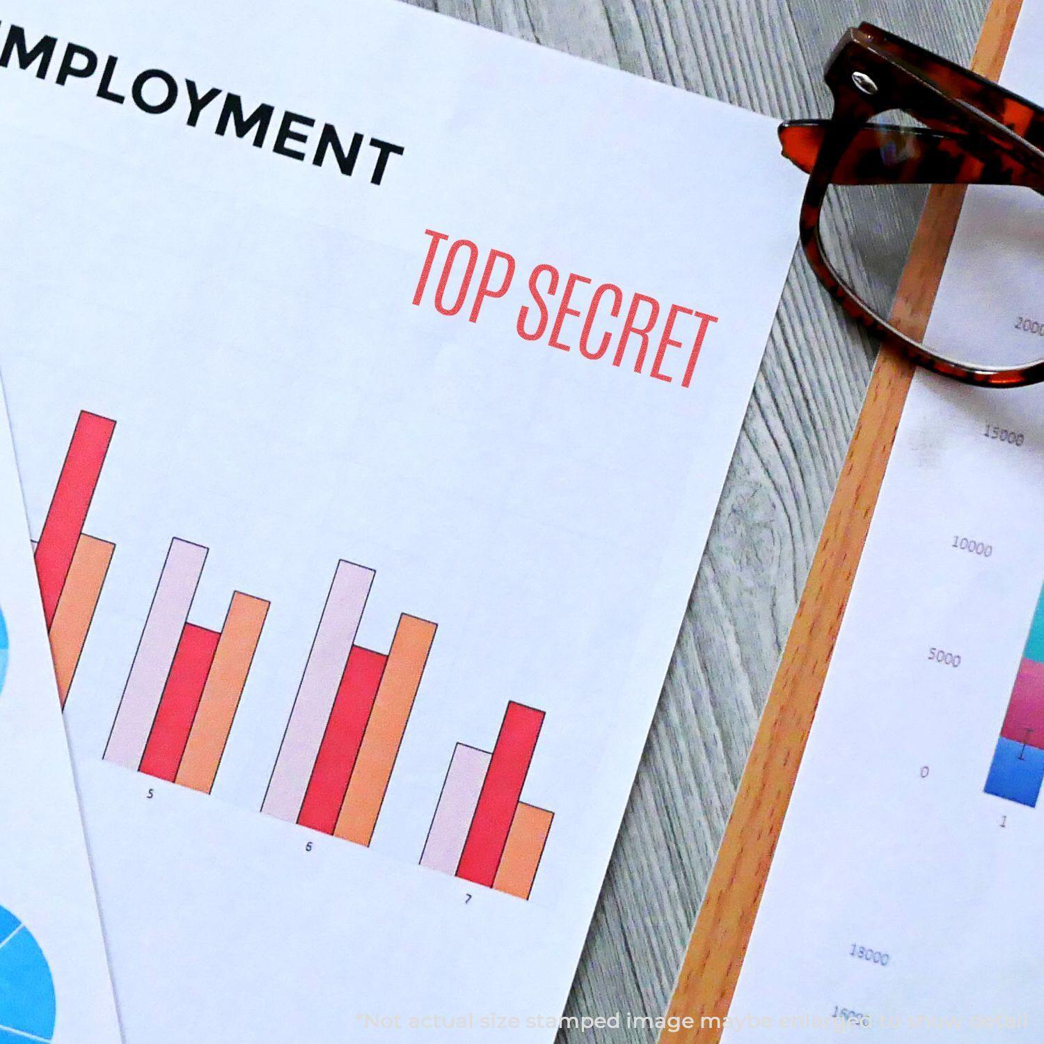 Top Secret Xstamper Stamp used on a document with charts and graphs, next to eyeglasses on a wooden desk.