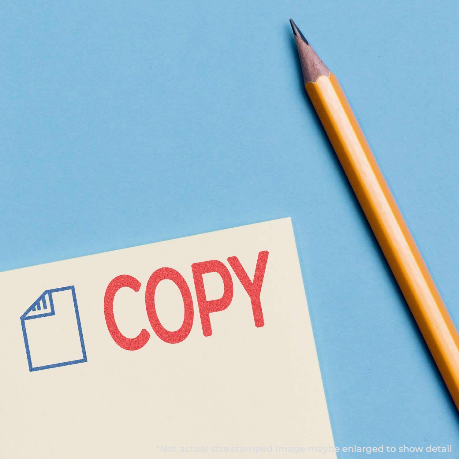 Two-Color Copy Xstamper Stamp imprint in red and blue on paper, next to a sharpened yellow pencil on a blue background.