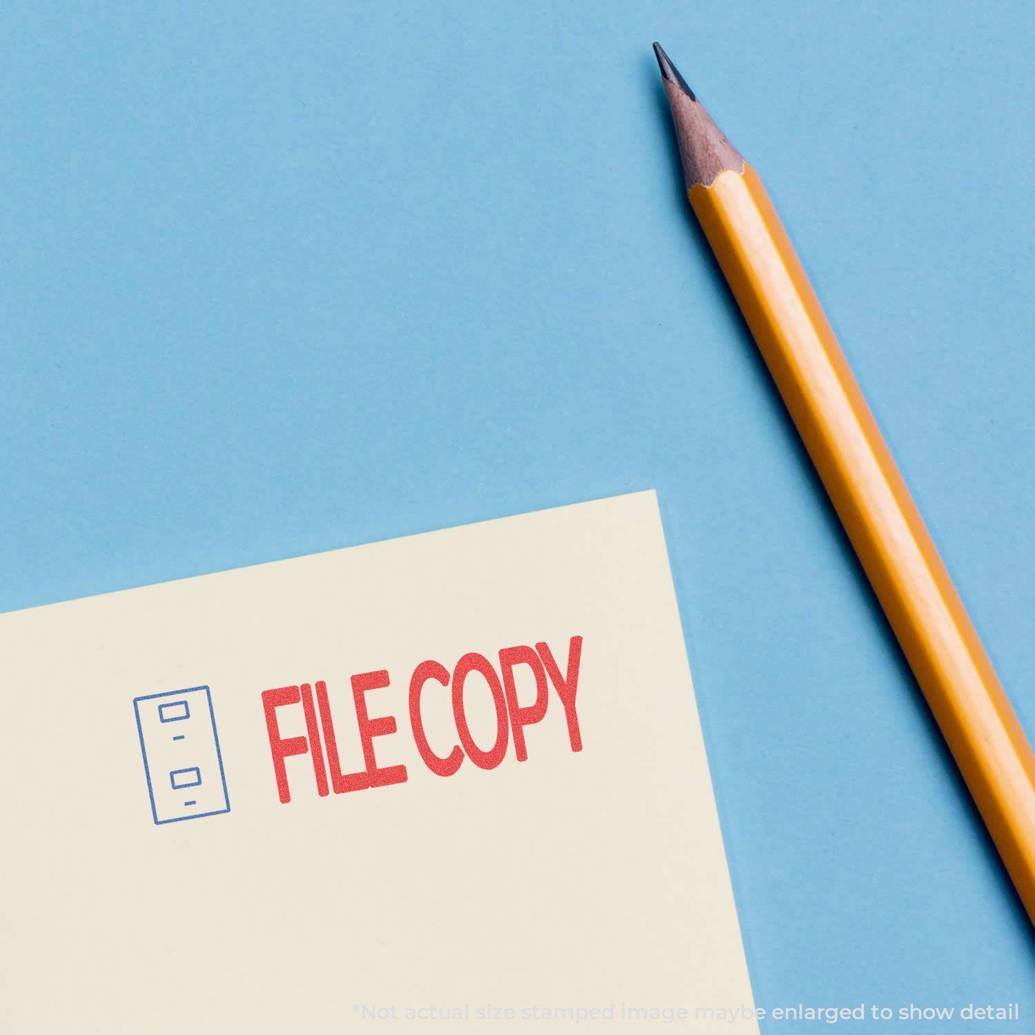 Two-Color File Copy Xstamper Stamp used on a yellow paper next to a sharpened pencil on a blue background.