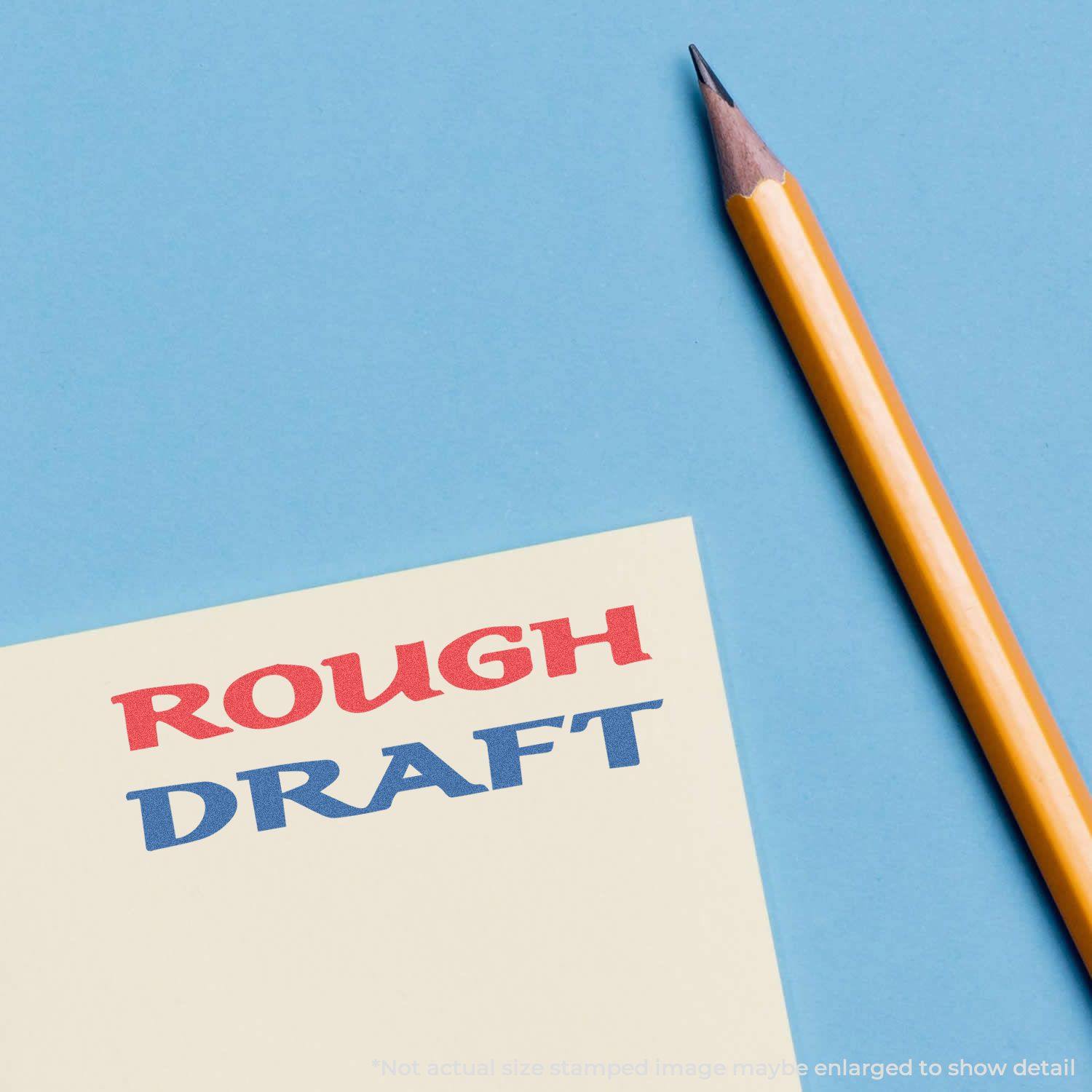 Two-Color Rough Draft Xstamper Stamp in use, showing ROUGH DRAFT stamped in red and blue on a yellow paper next to a pencil on a blue background.