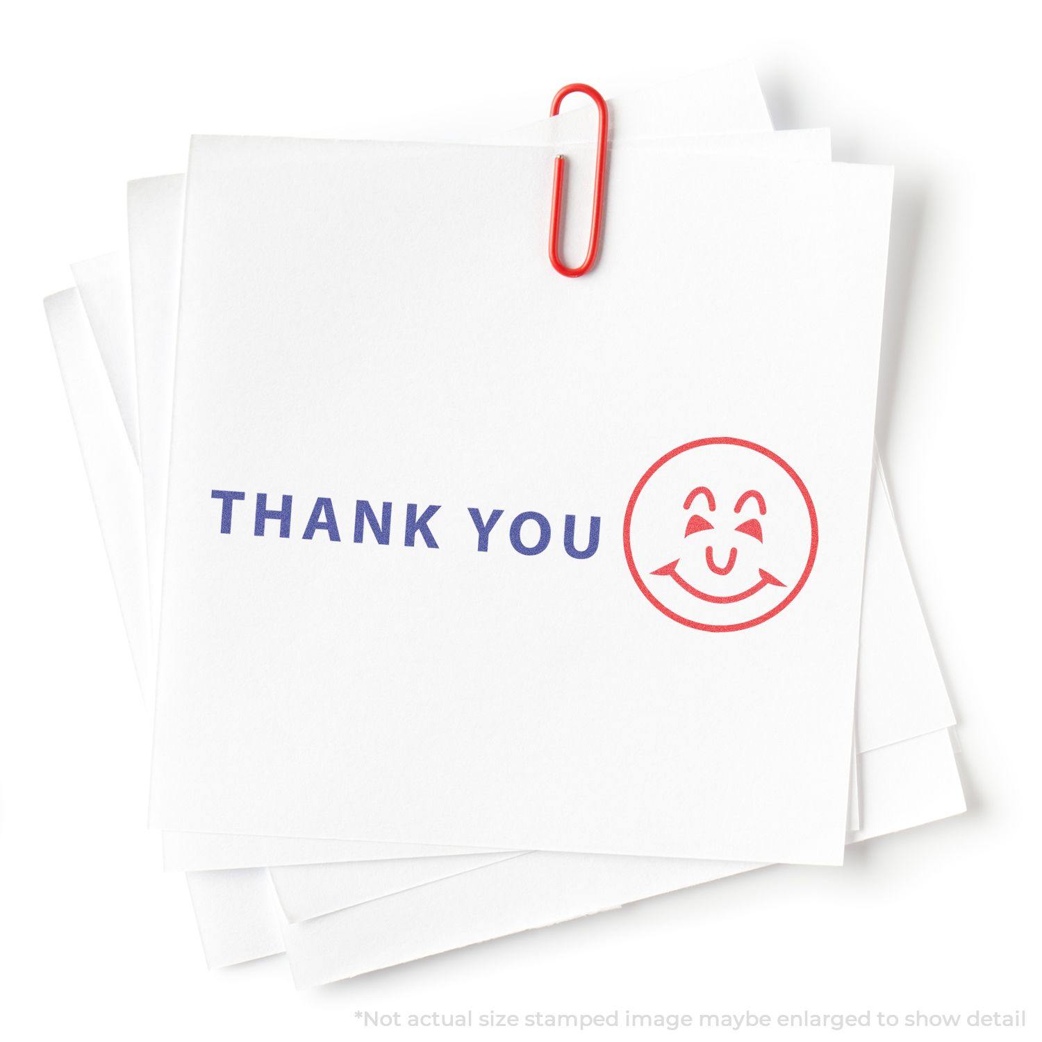 Two-Color Thank You Xstamper Stamp on white paper with a red smiley face and blue THANK YOU text, held by a red paperclip.