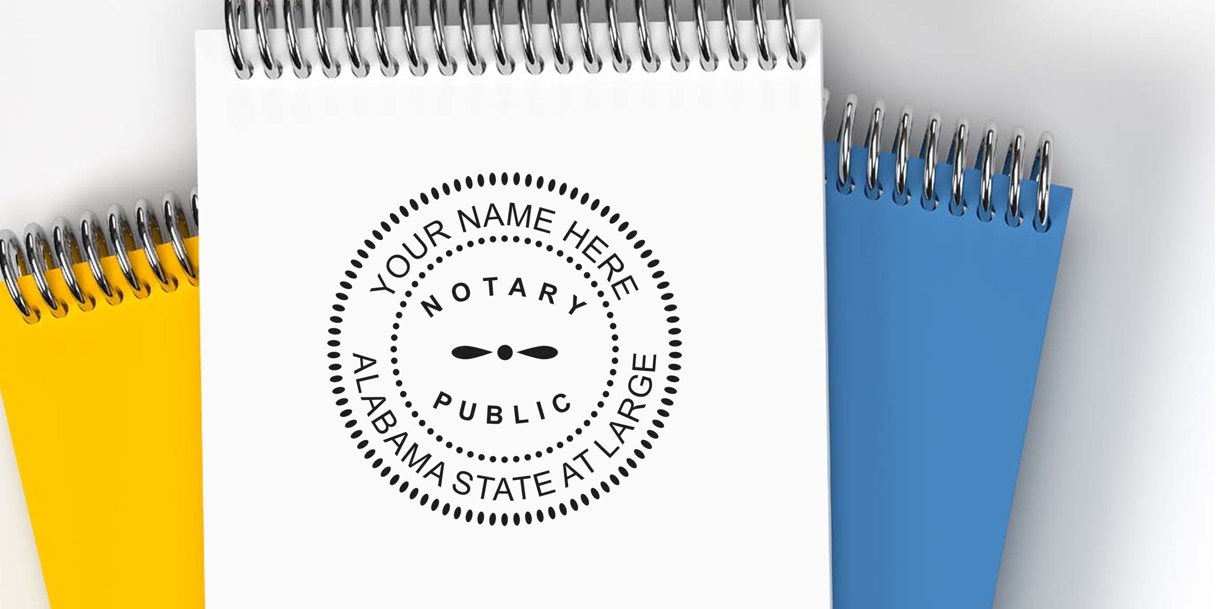 Top-down view of spiral-bound notebooks in white, yellow, and blue featuring a black circular notary public seal graphic on the white cover reading "Your Name Here, Alabama State At Large."