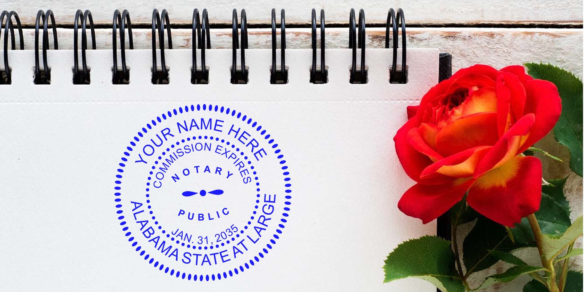 Blue circular Alabama notary seal stamped on white spiral notebook page beside a vibrant red and yellow rose on wooden background