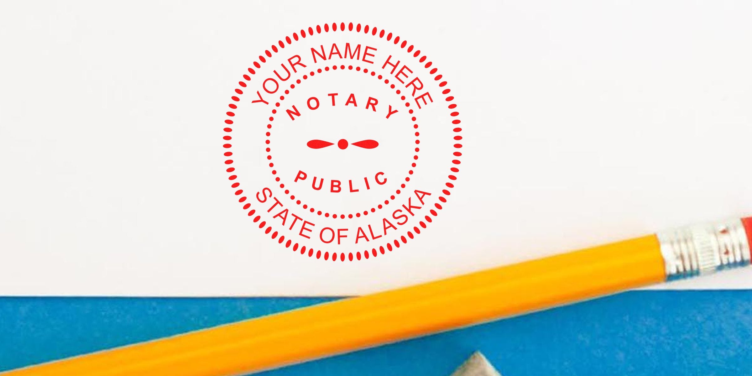 Red circular Alaska notary public stamp reading "Your Name Here" on white paper, close-up with a yellow pencil and blue folder at the bottom, office stationery for notarization and document signing.