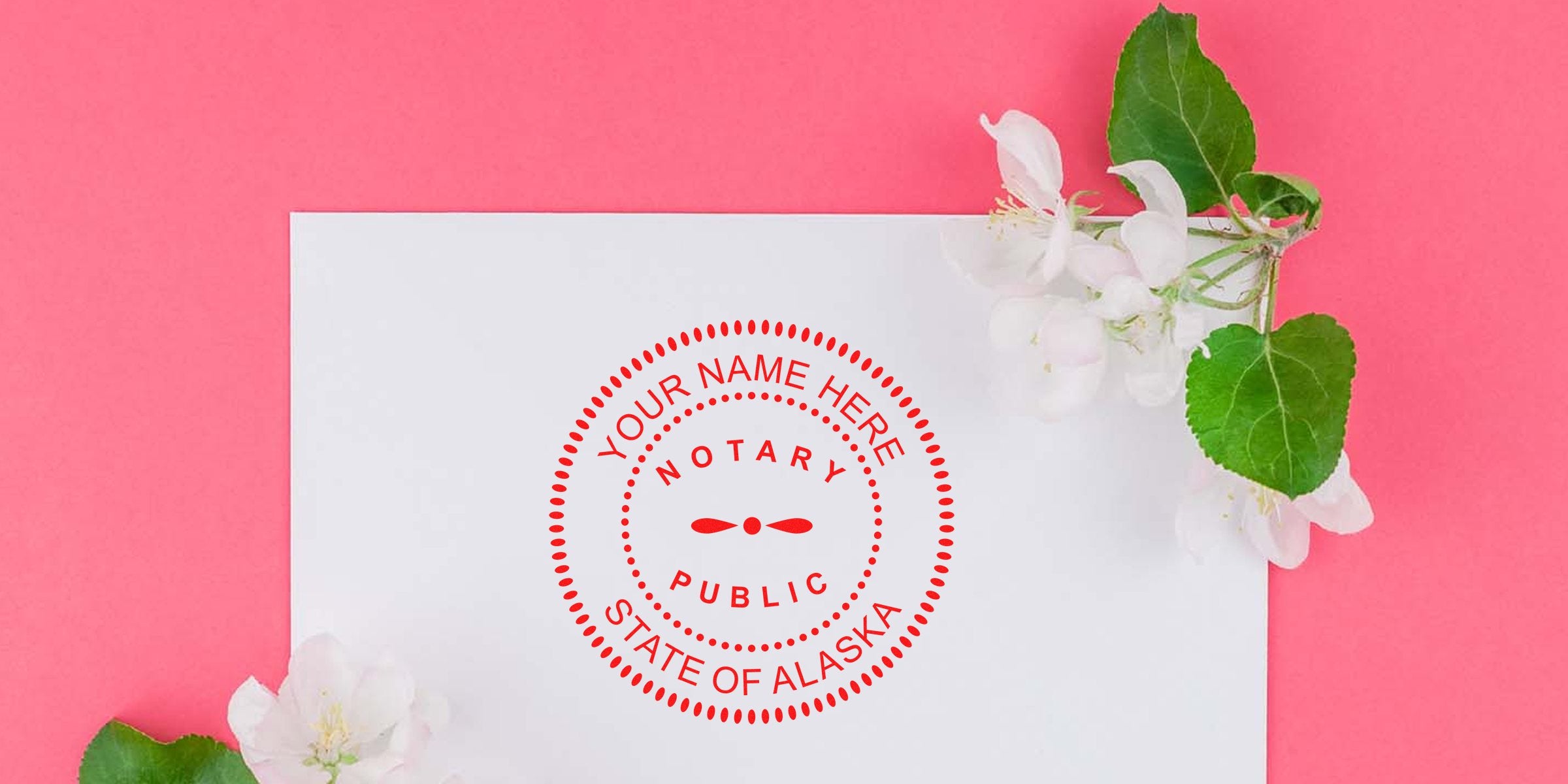 White paper on pink background with red "Notary Public State of Alaska" circular seal mockup reading "Your Name Here," accented by white spring blossoms and green leaves.