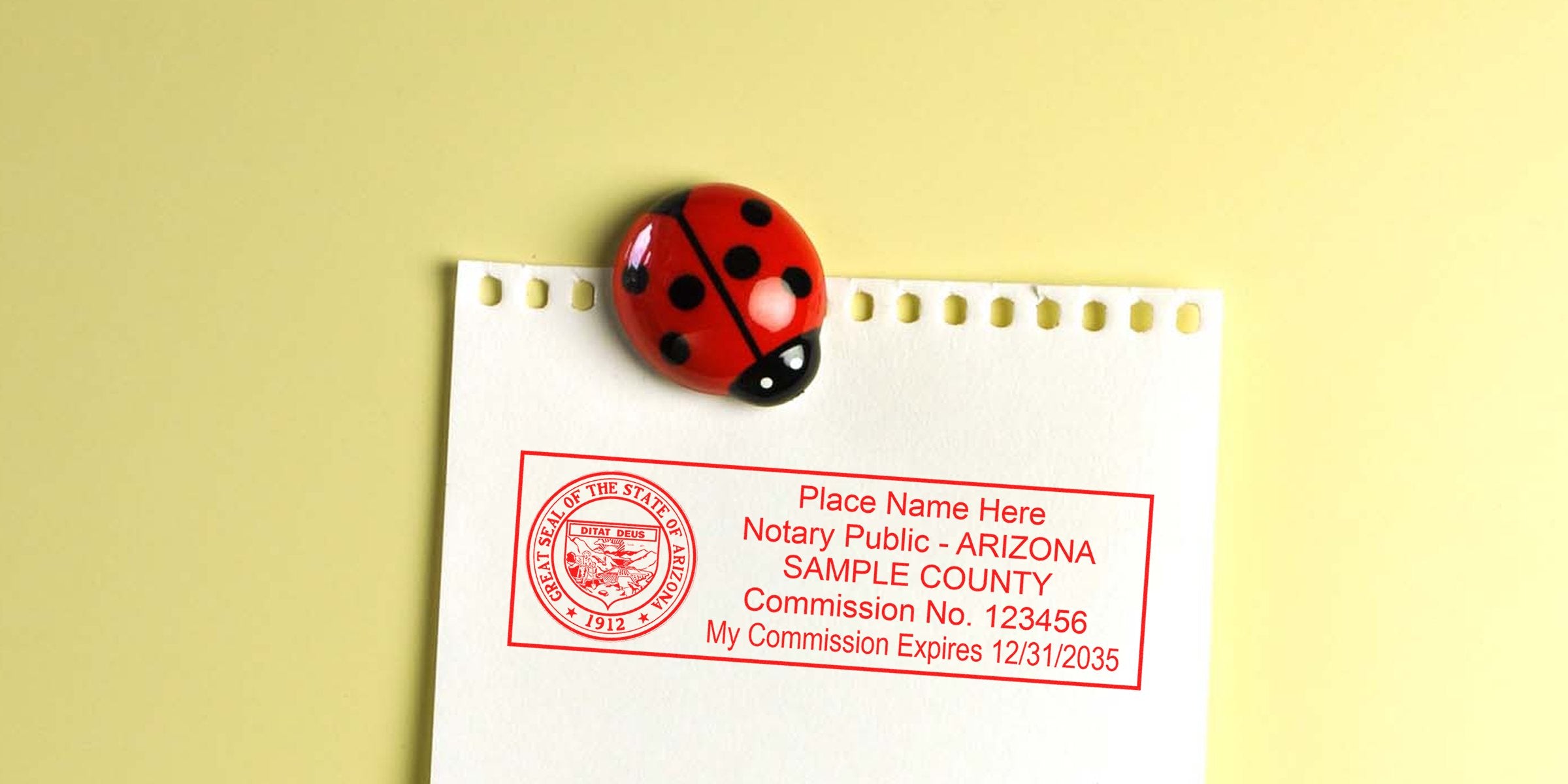 Close-up of a torn notebook page held by a red ladybug magnet featuring a red Arizona notary public sample stamp with commission info.