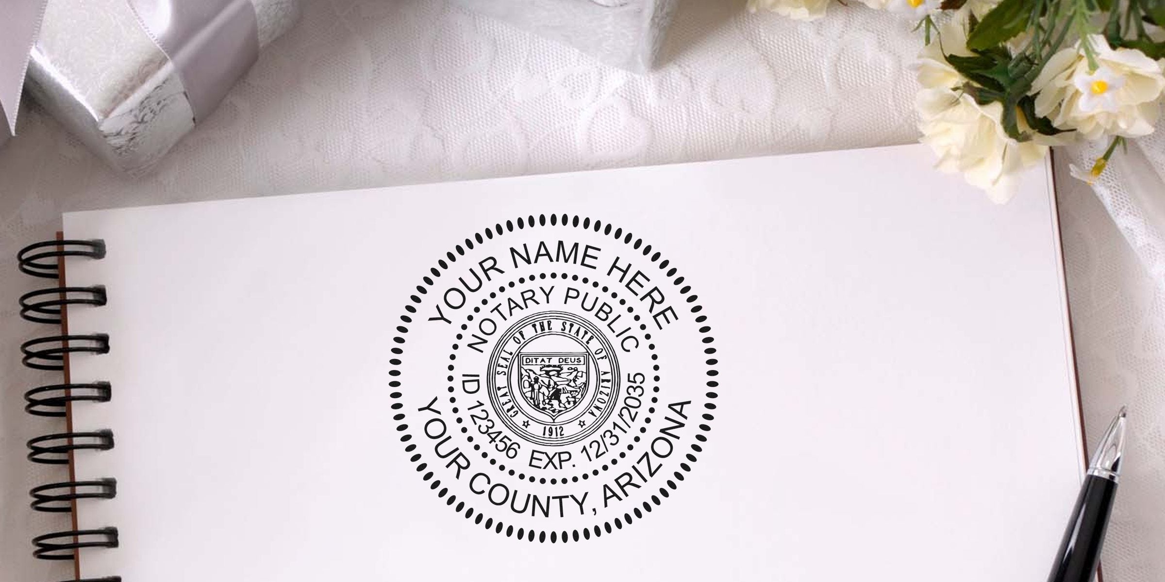 Mockup of a custom Arizona notary public seal stamped on a spiral notebook page, showing placeholder "Your Name Here", ID/exp info, with pen and decorative flowers nearby.