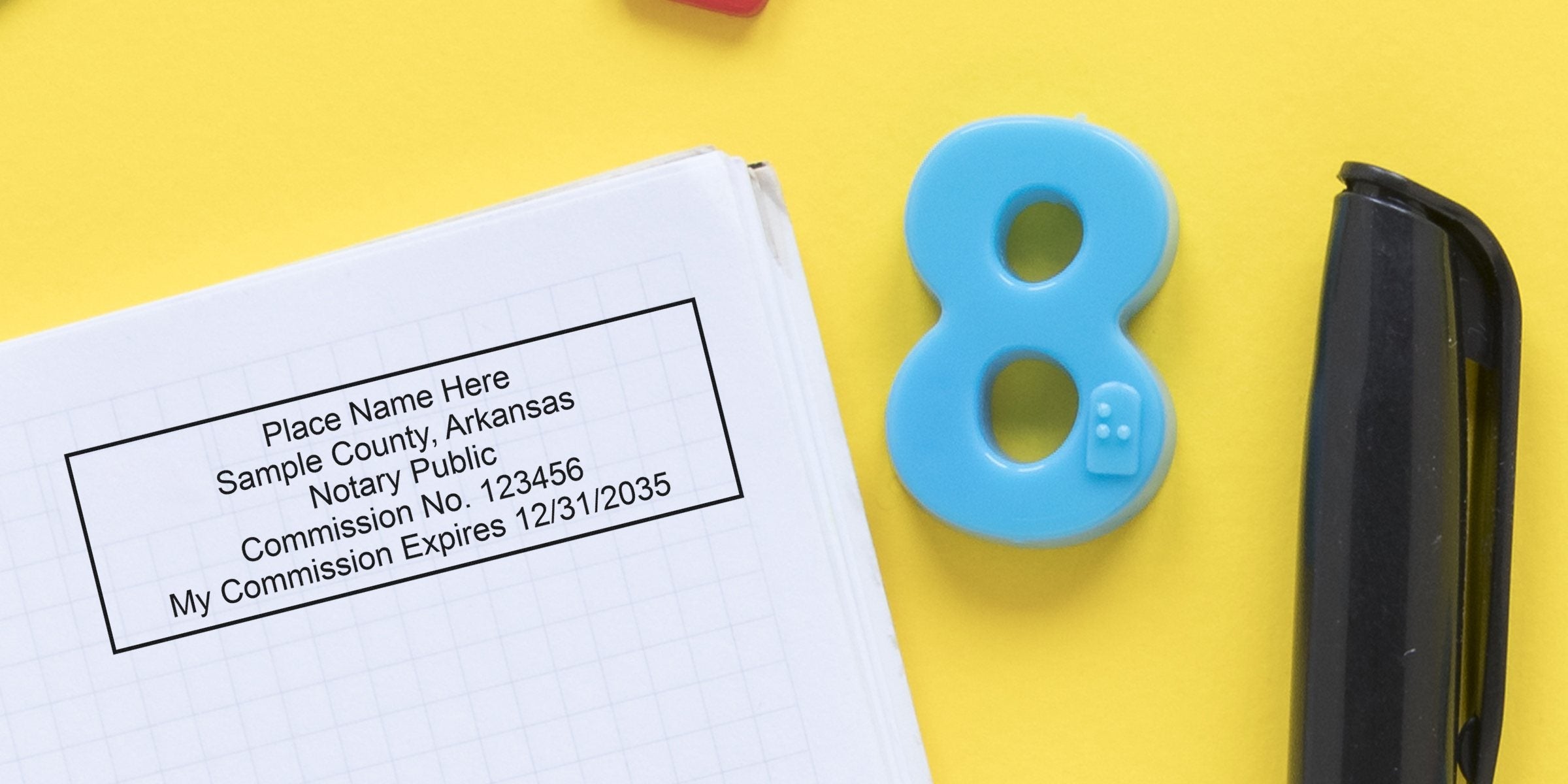 Top-down view of a notary commission stamp imprint on graph paper beside a blue plastic number 8 toy and a black pen on a bright yellow background, stationery and notary paperwork concept.